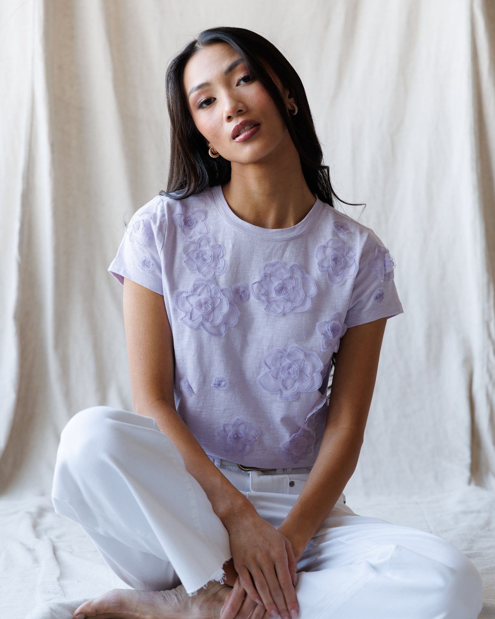 Woman wearing a light purple t-shirt with floral patterns and white pants against a neutral background