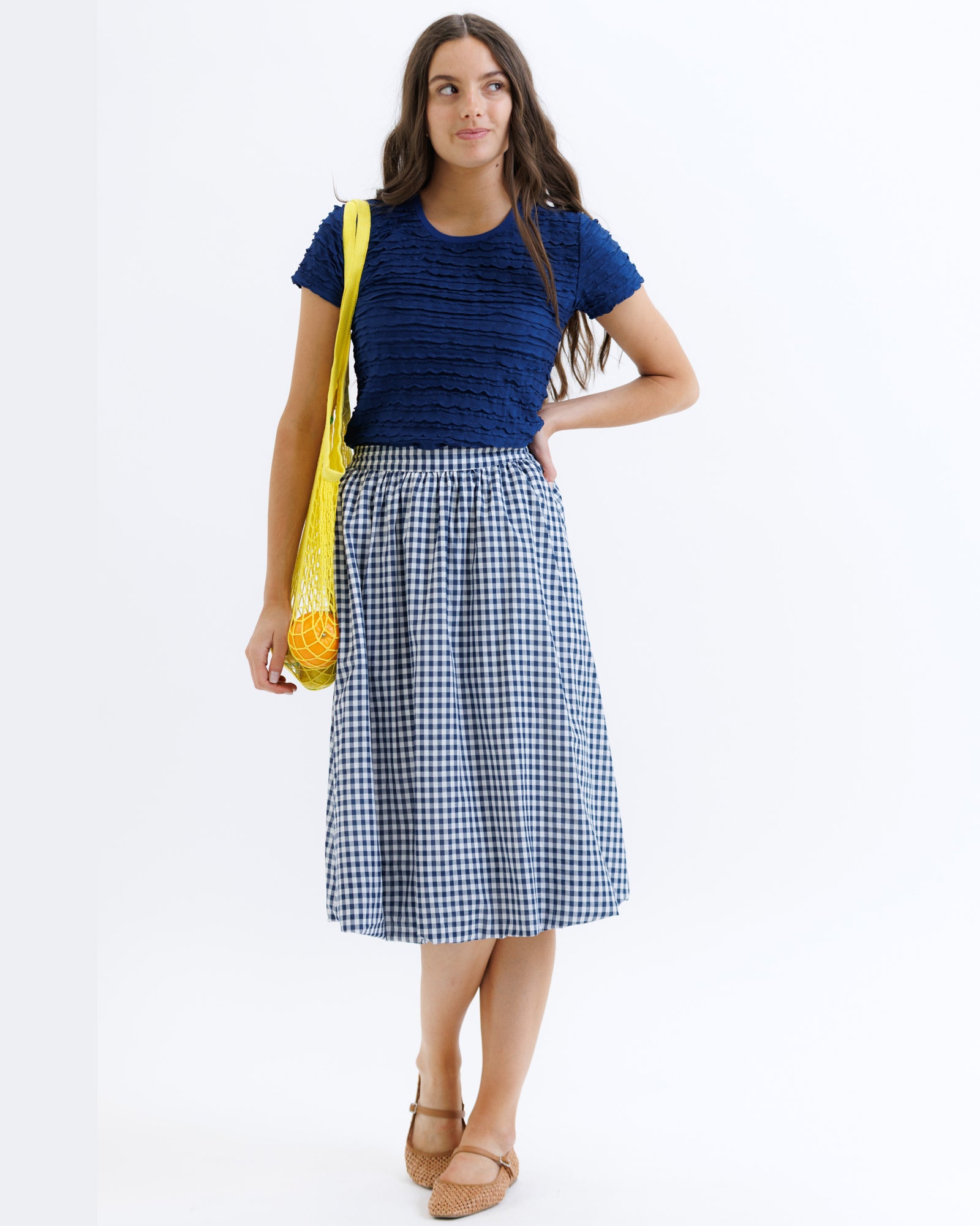 Woman wearing a blue top and checkered skirt with a yellow bag on a white background