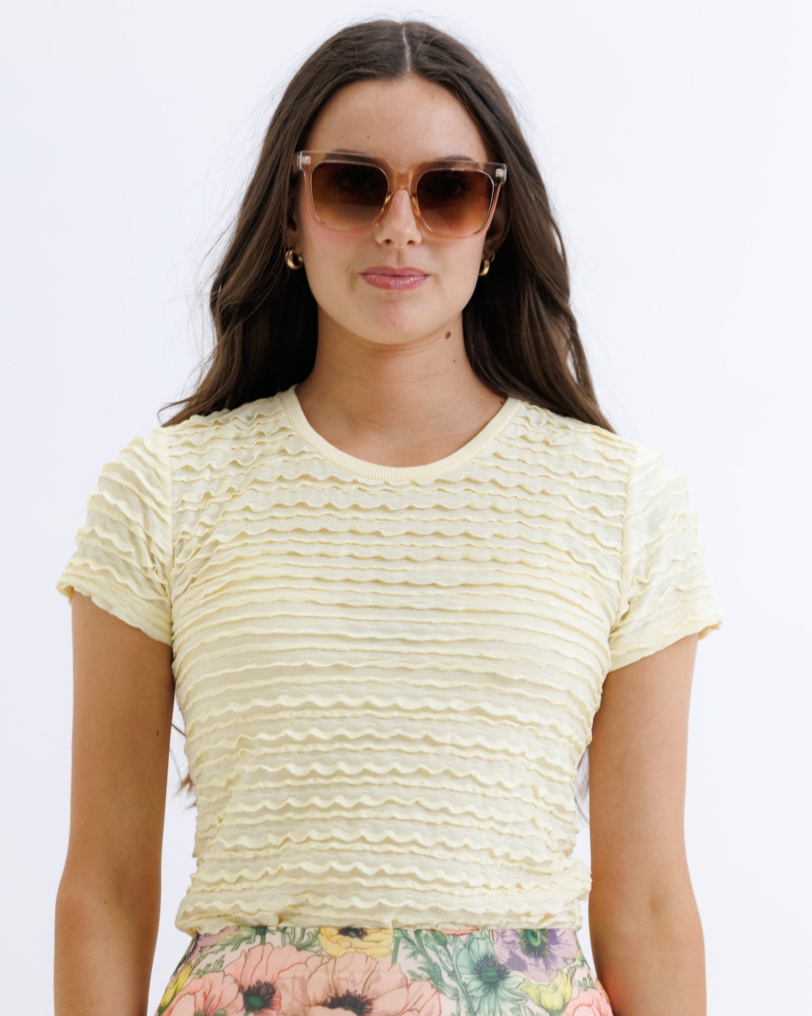 Woman wearing a yellow textured top and floral pants on a white background
