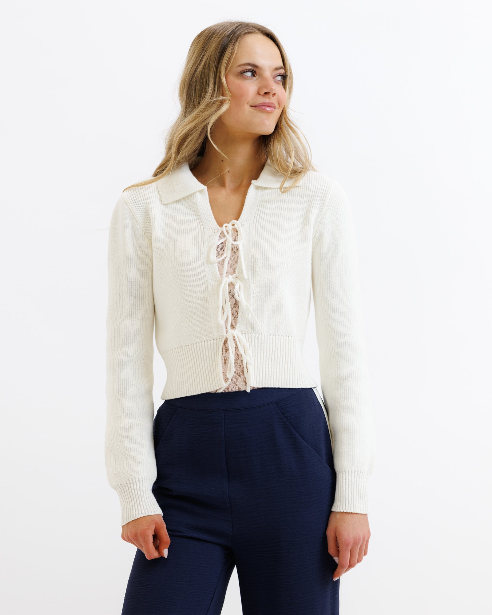 Woman wearing a white cardigan over a lace top with navy pants on a white background