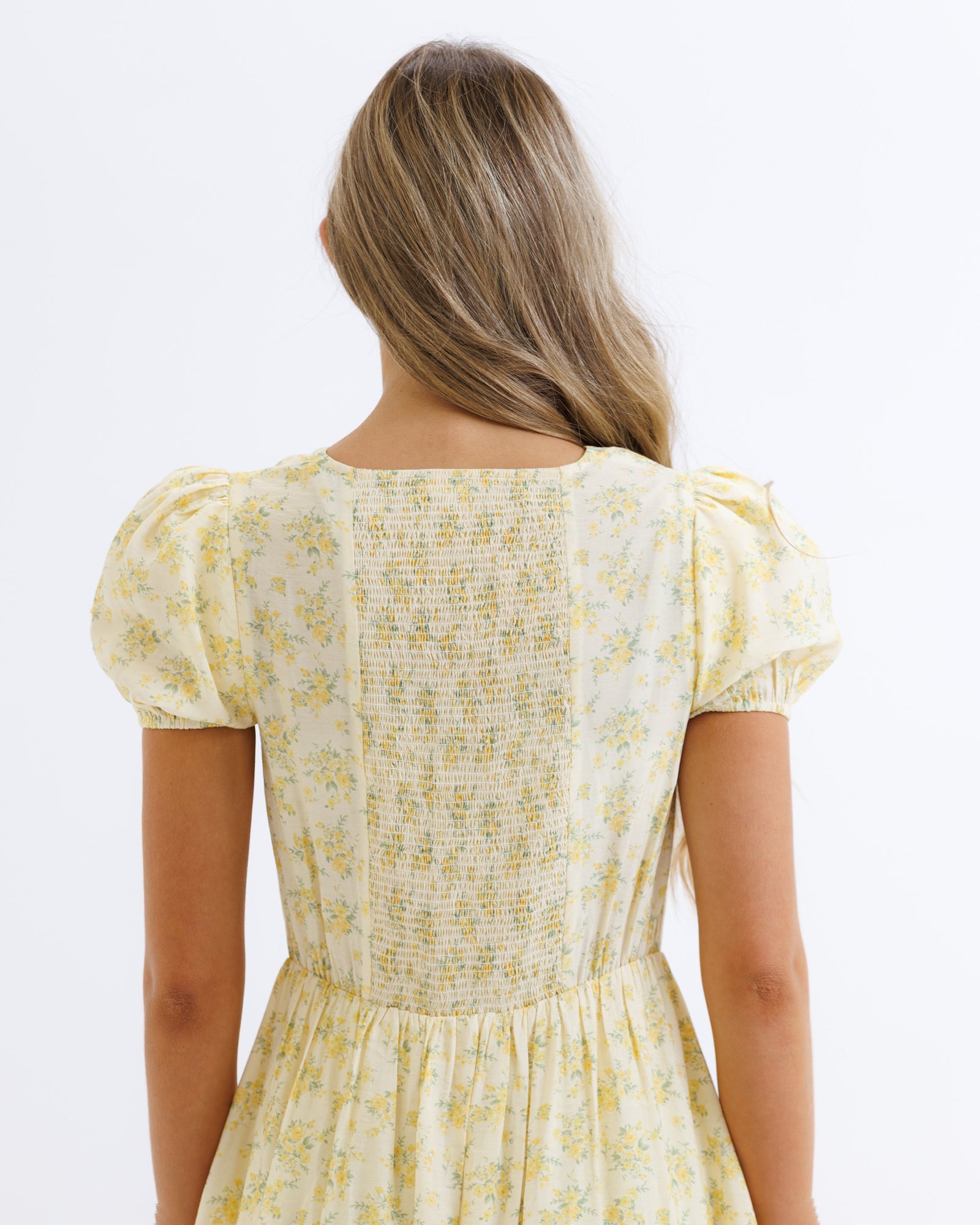 Woman wearing a yellow floral dress on a white background
