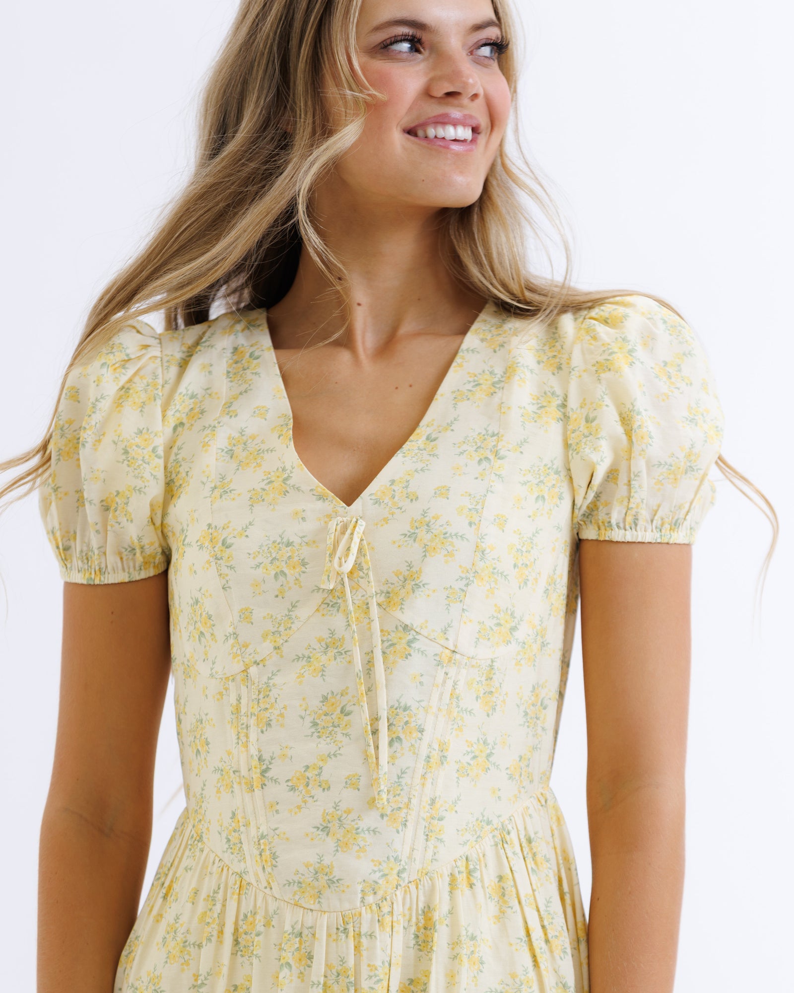 Woman wearing a yellow floral dress against a white background