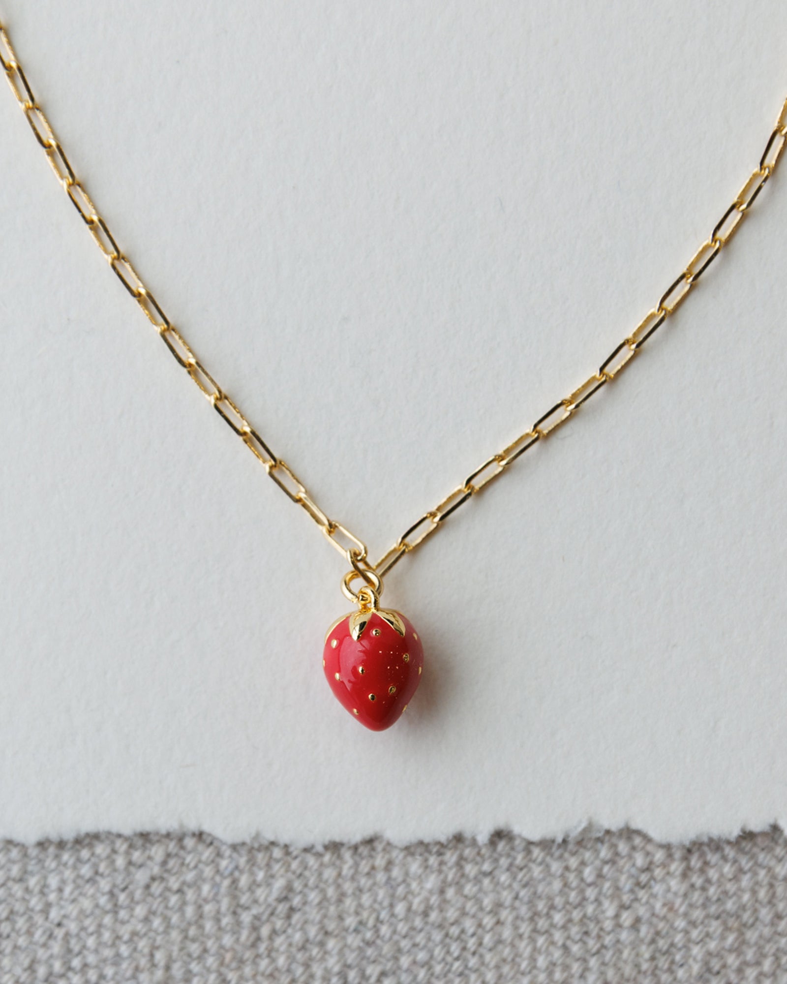 Gold necklace with a red strawberry pendant on a light gray background