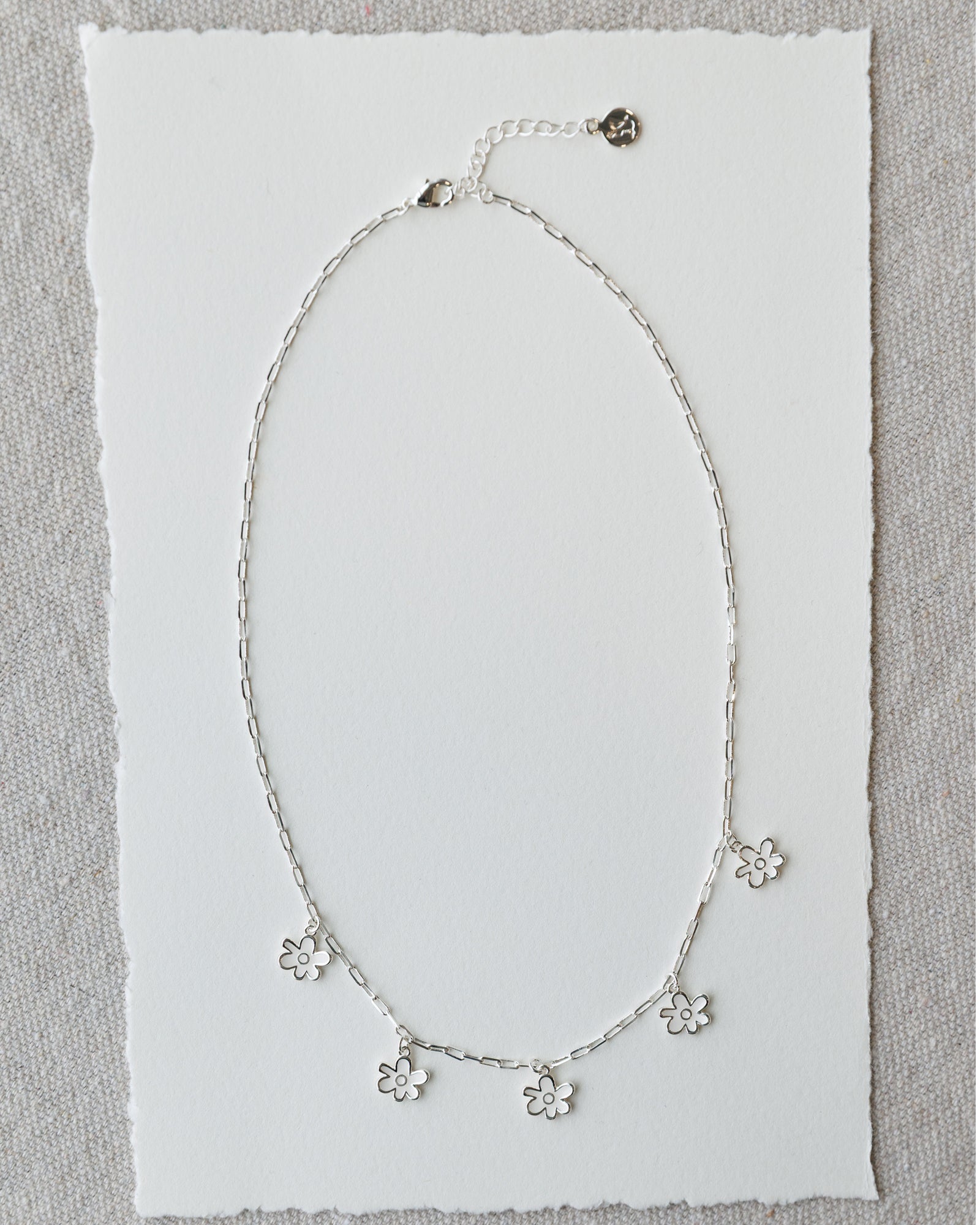 Silver necklace with floral pendants on a textured white background