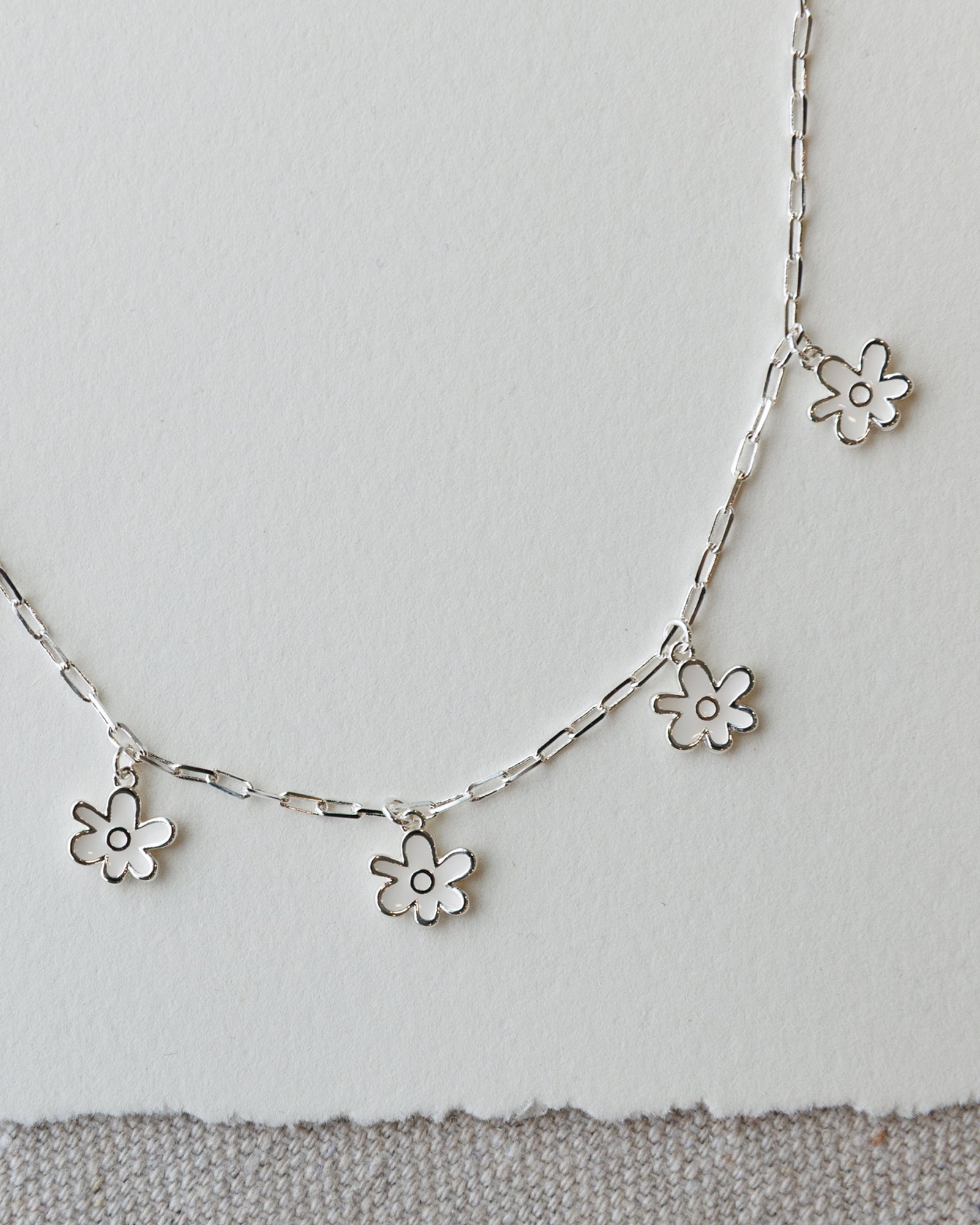 Silver necklace with flower pendants on a light gray background