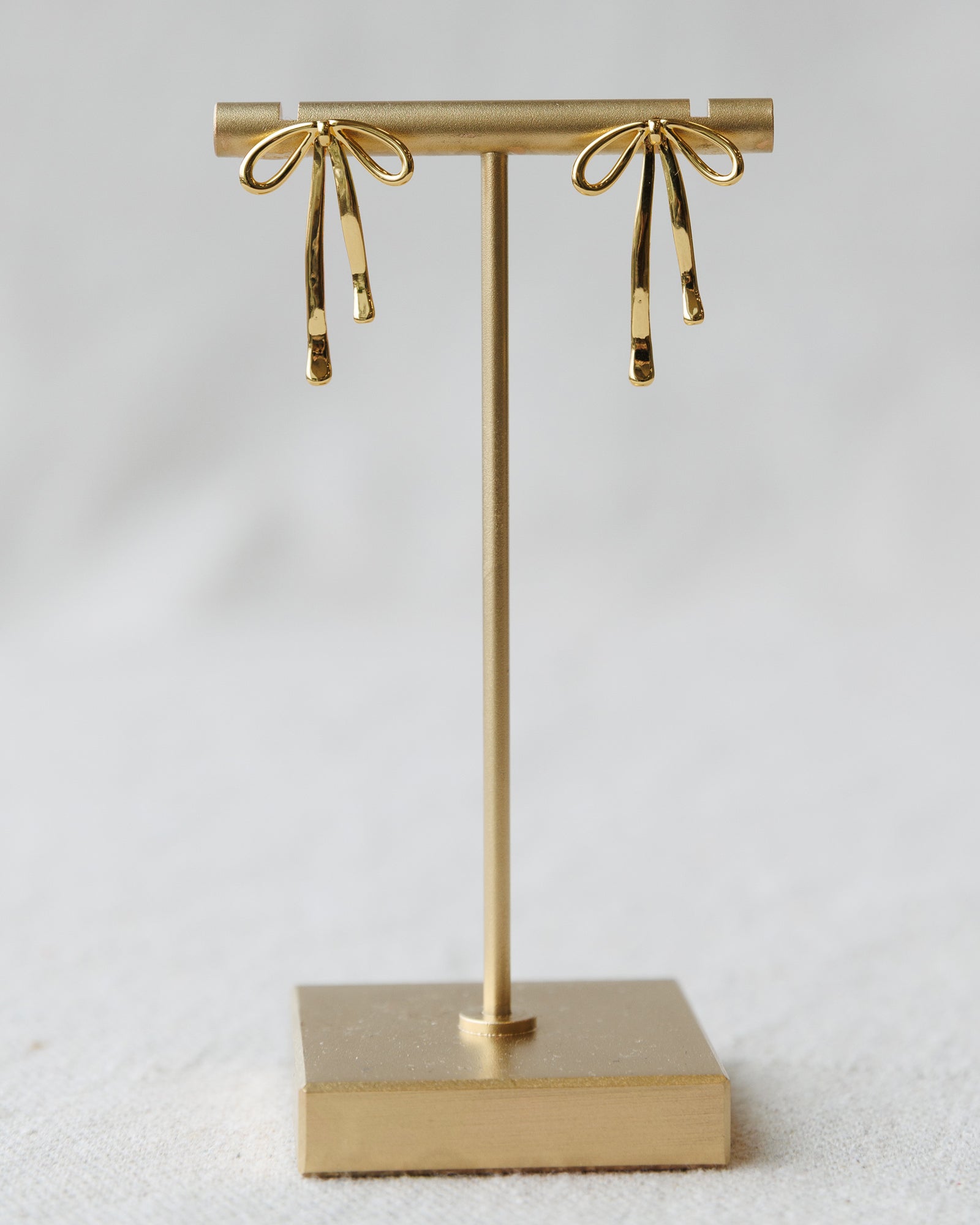 Gold earring stand with bow-shaped earrings on a light gray background