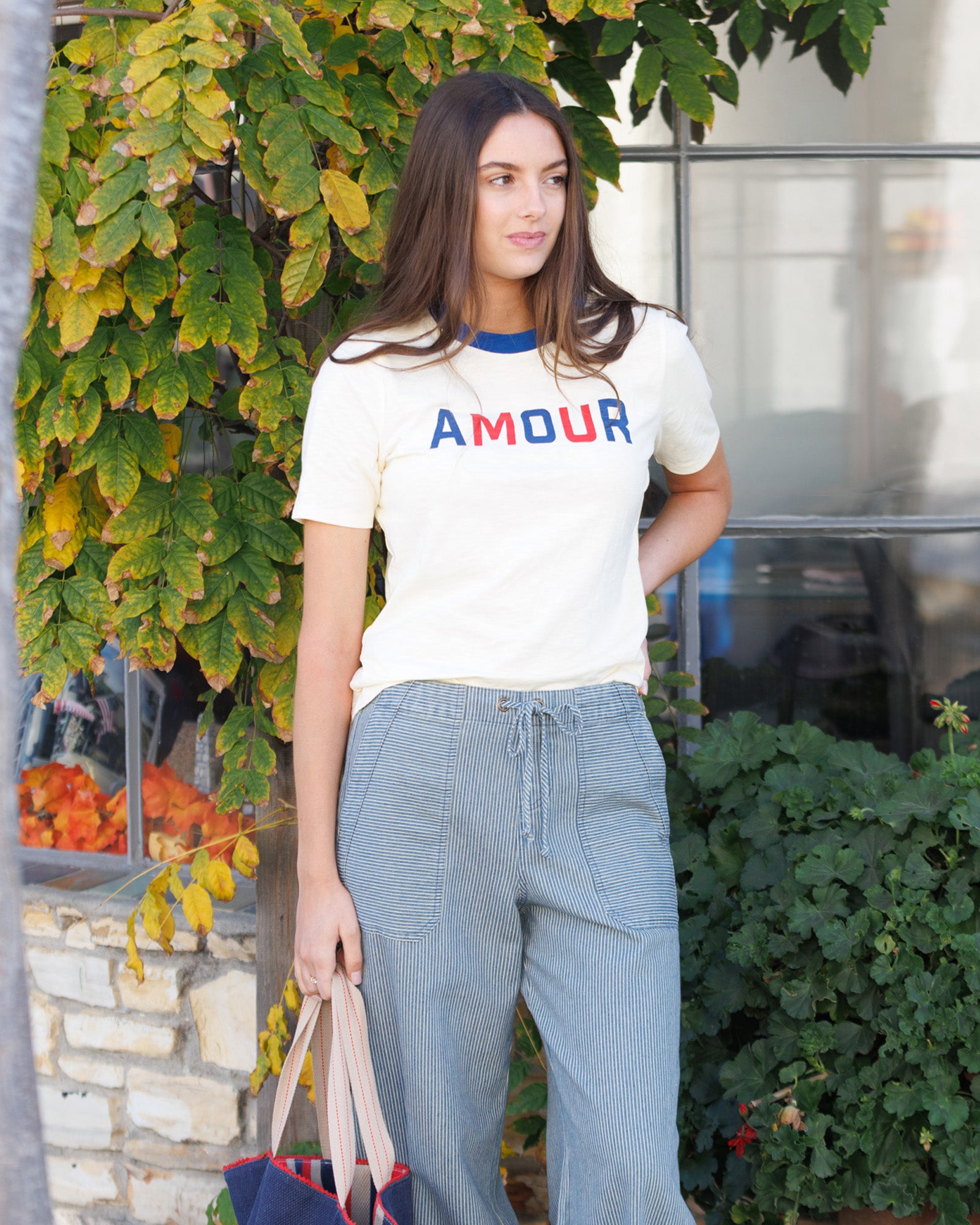 Woman wearing a 'AMOUR' t-shirt standing outdoors with greenery around.