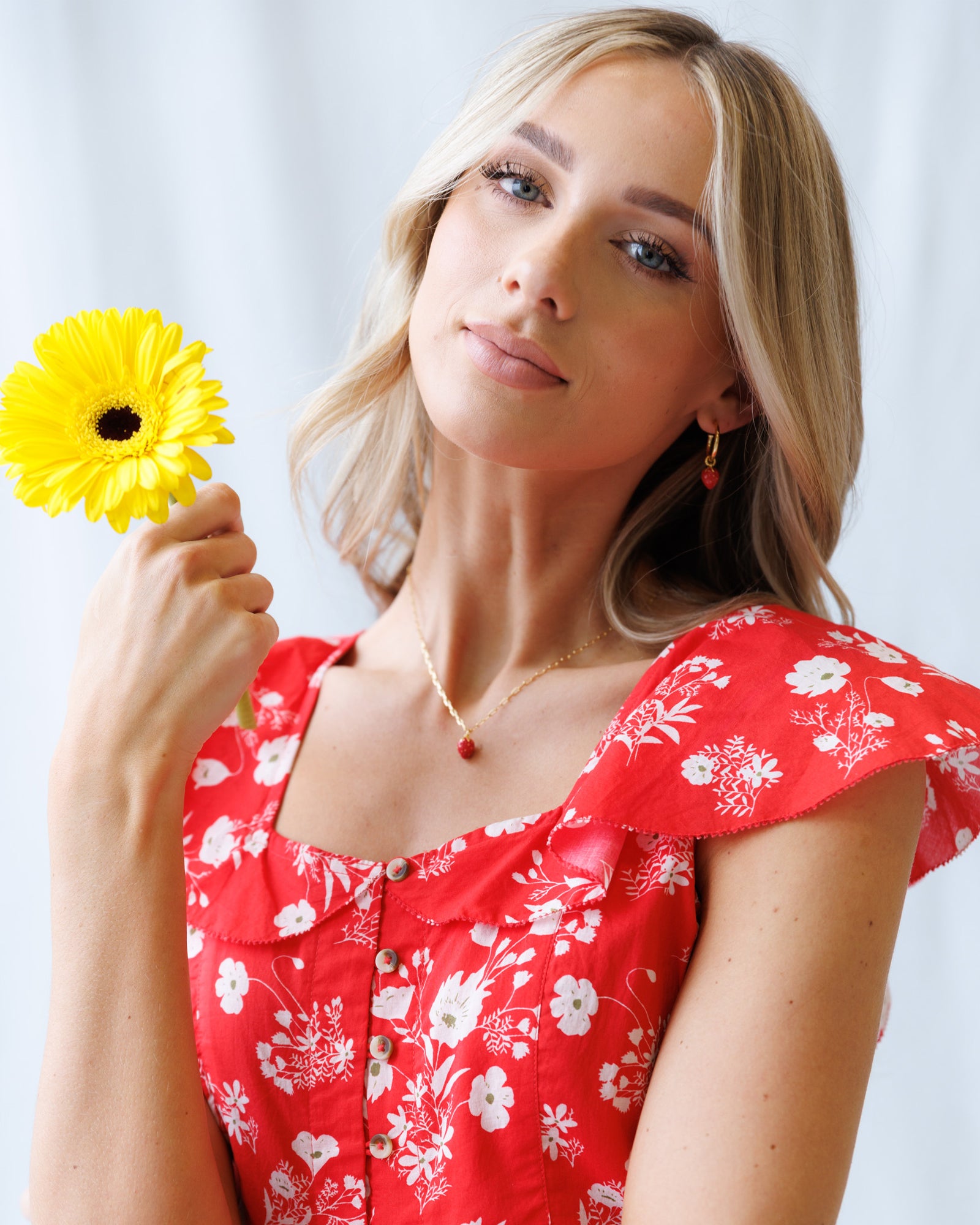 Woman in a red floral dress holding a yellow flower against a white background