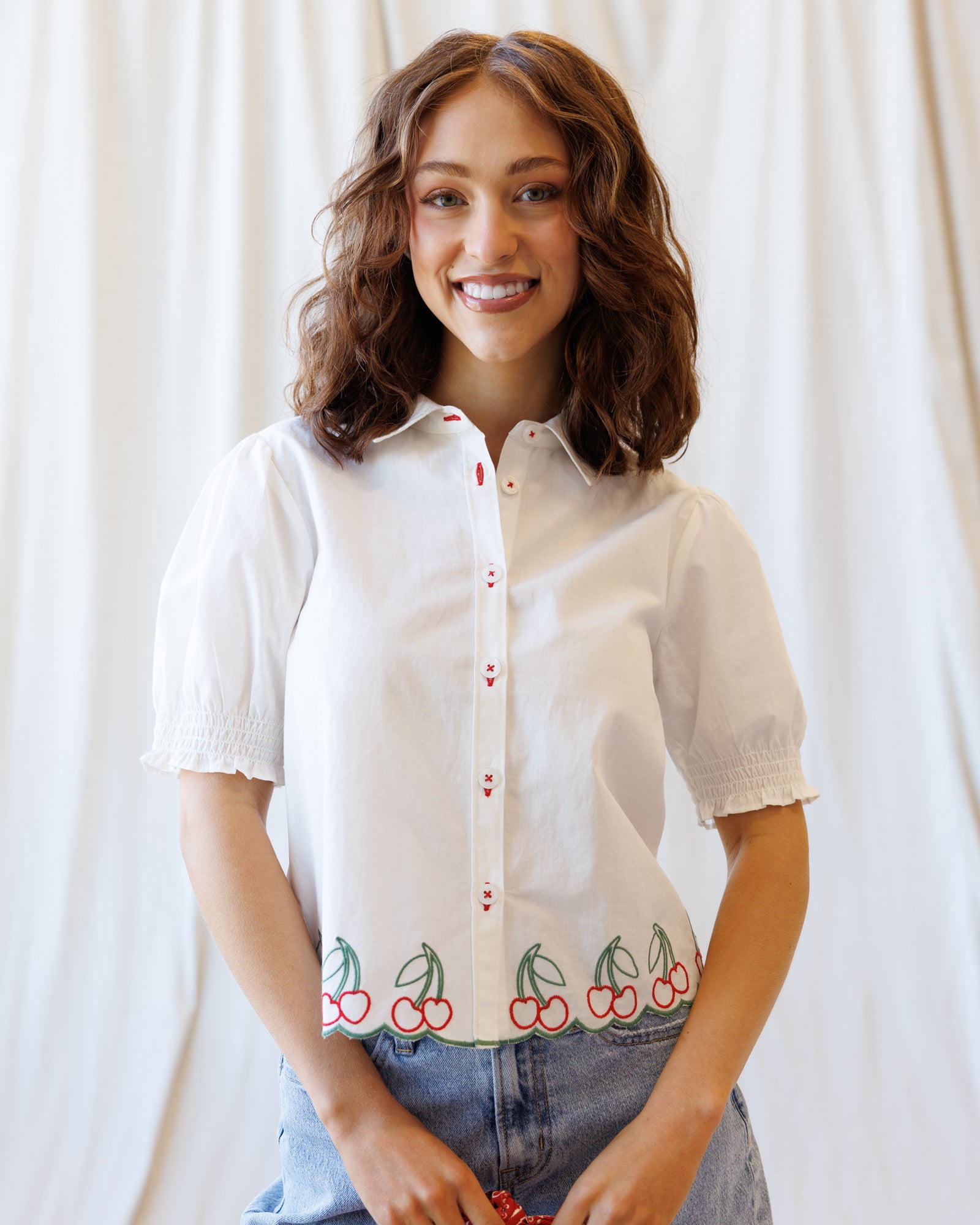 Woman wearing a white shirt with cherry design against a plain background