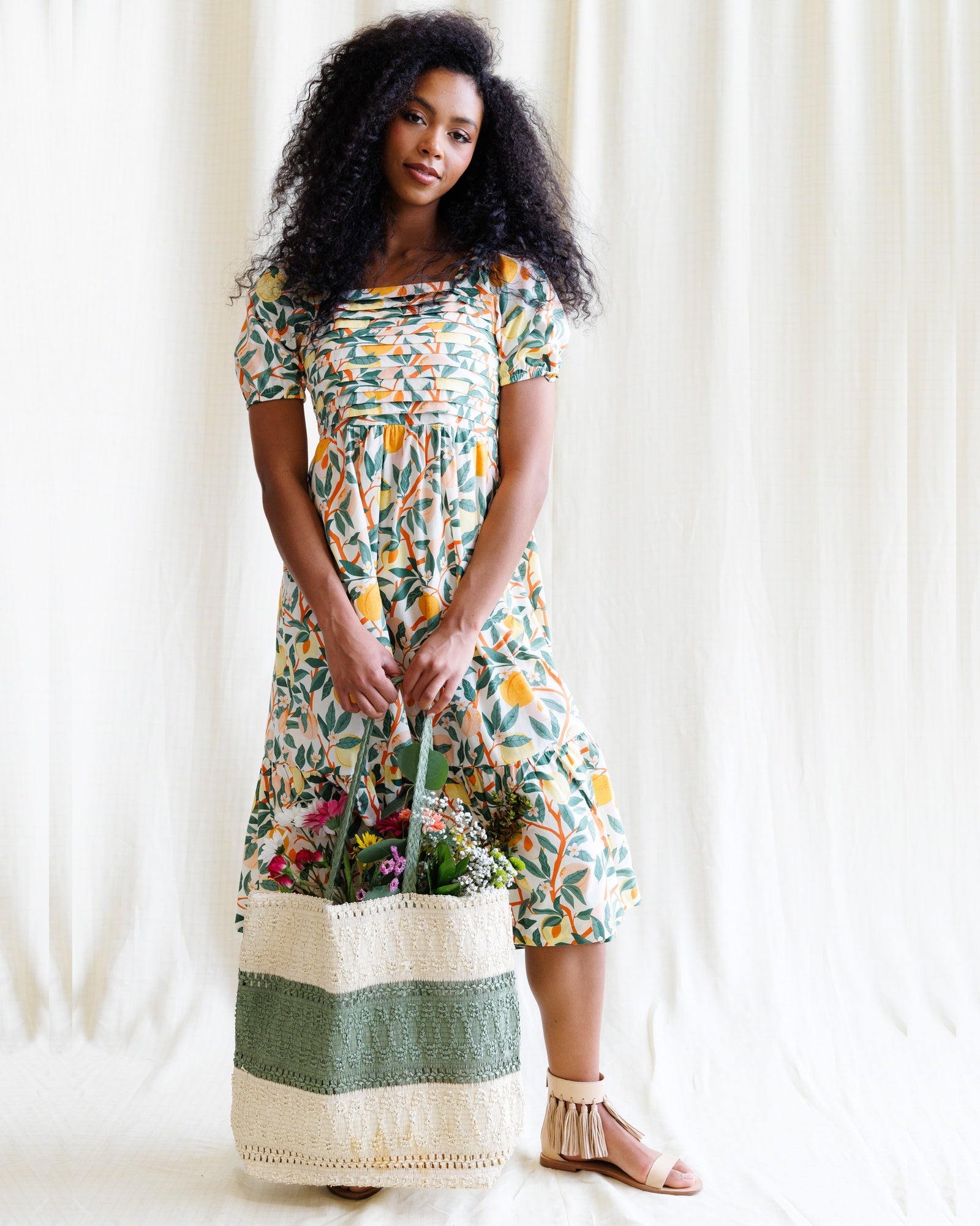 Woman wearing a floral dress holding a basket against a white curtain background