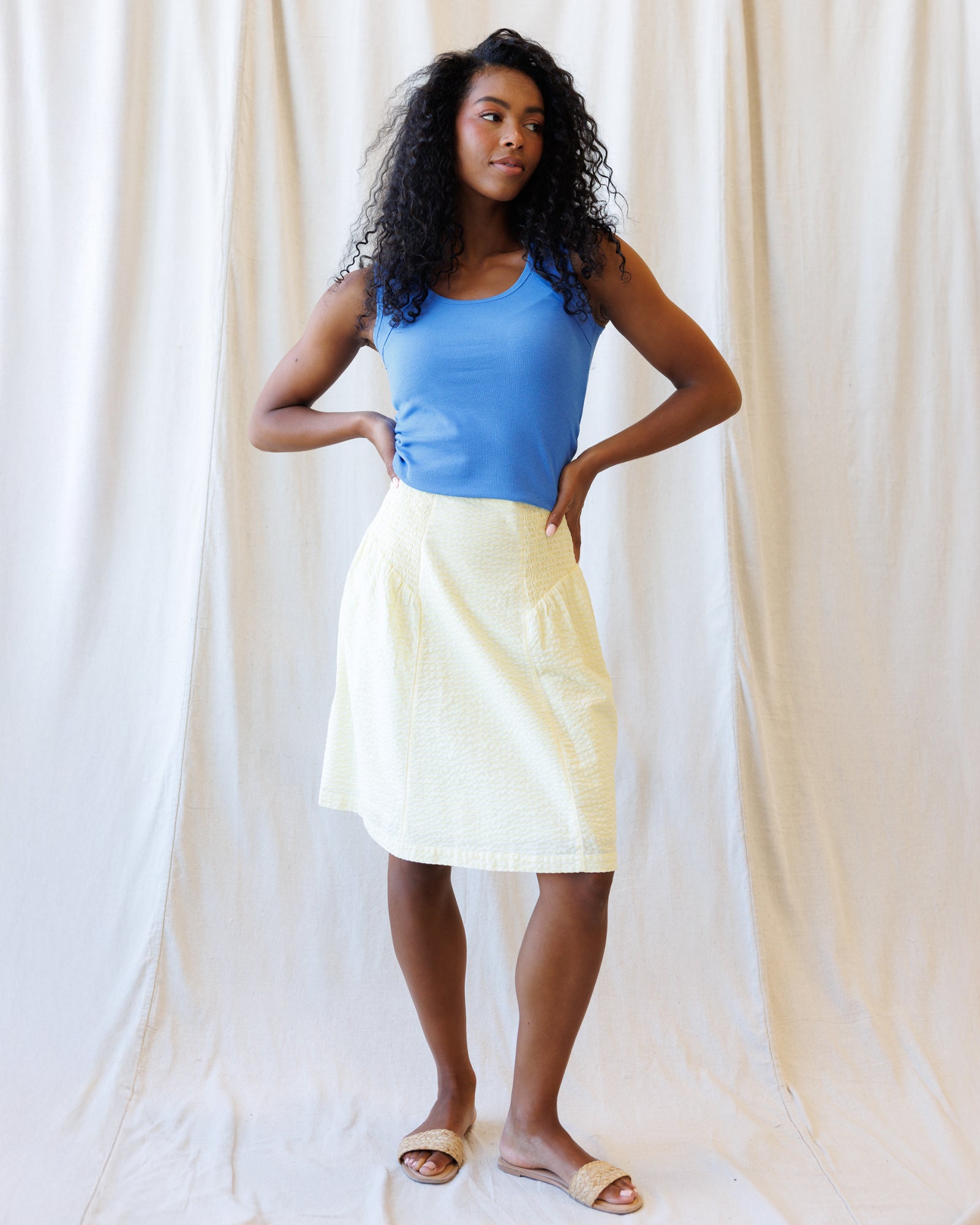 Woman wearing a blue top and yellow skirt against a white curtain background