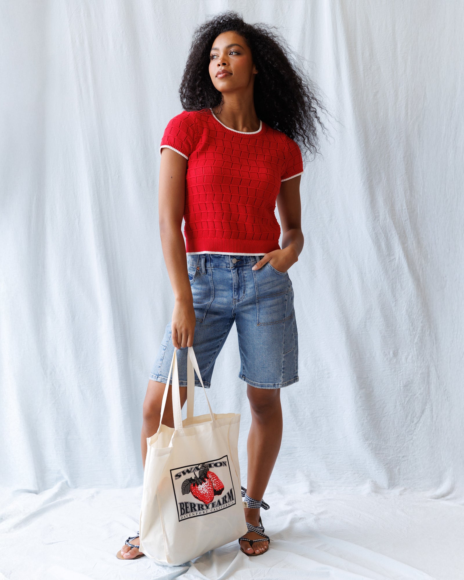 Woman wearing a red sweater with blue jeans against a plain background
