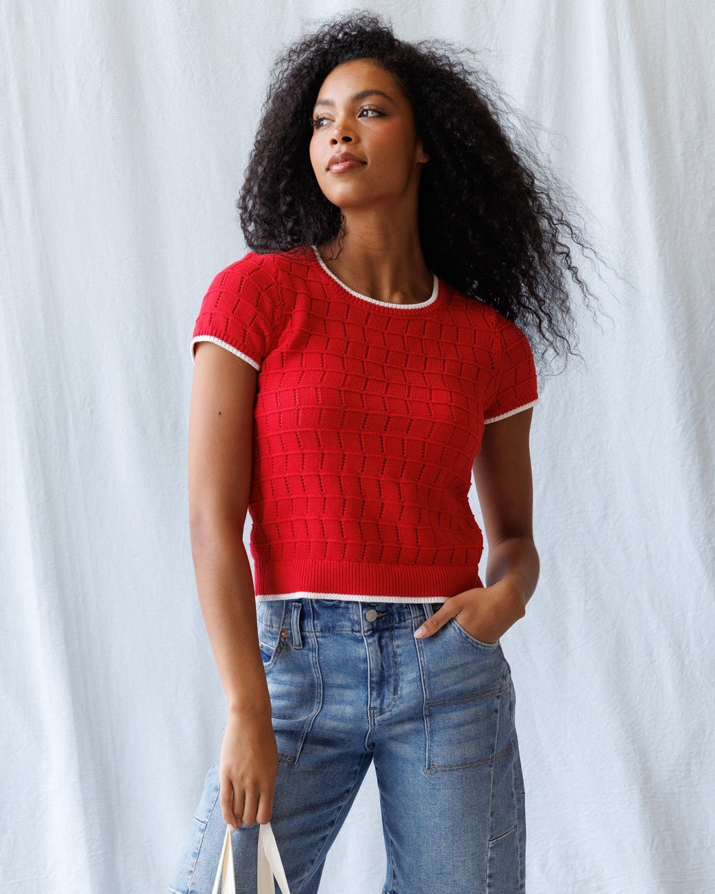 Woman in a red top and denim shorts holding a tote bag against a white background