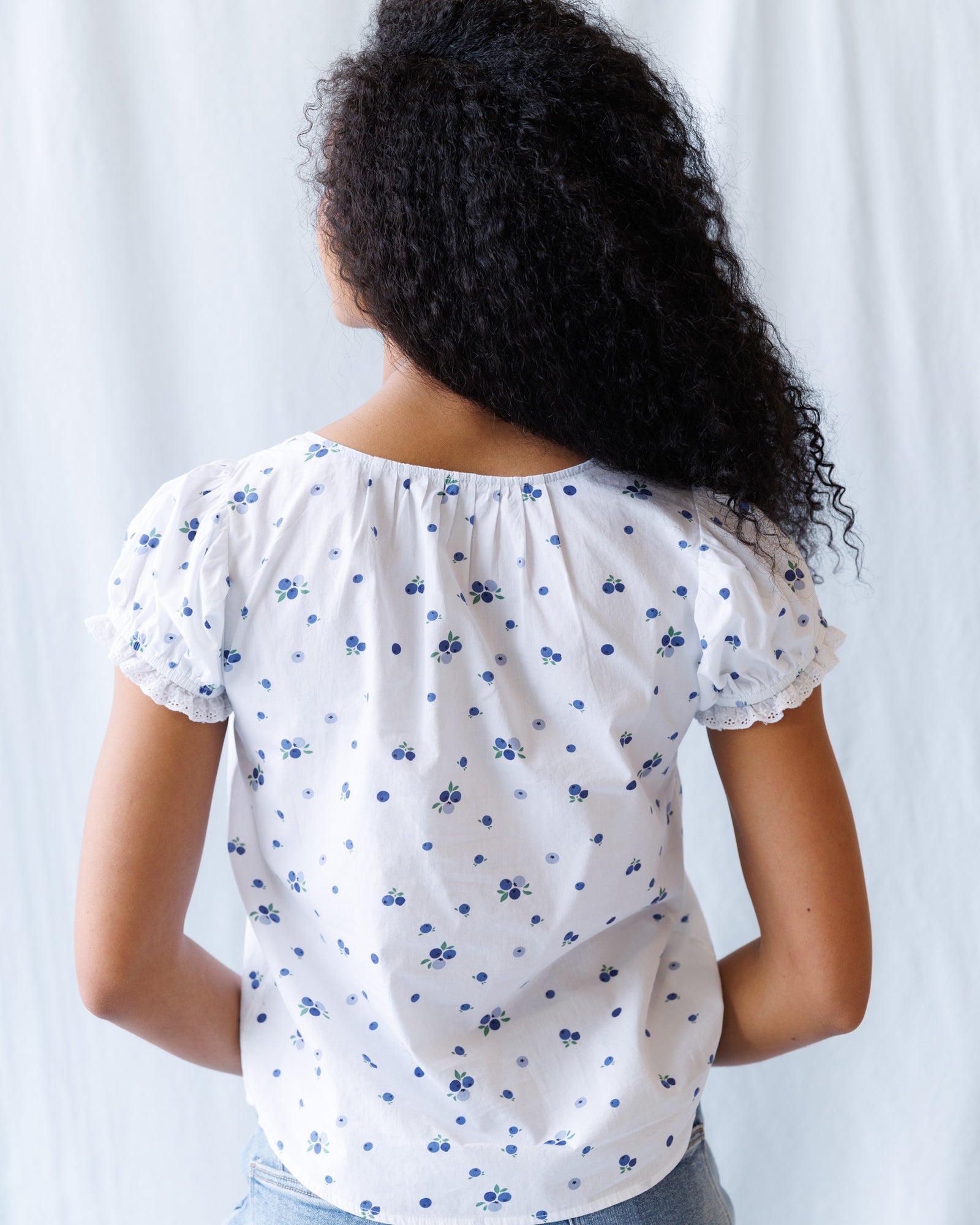 Person wearing a white blouse with blue floral patterns against a light background