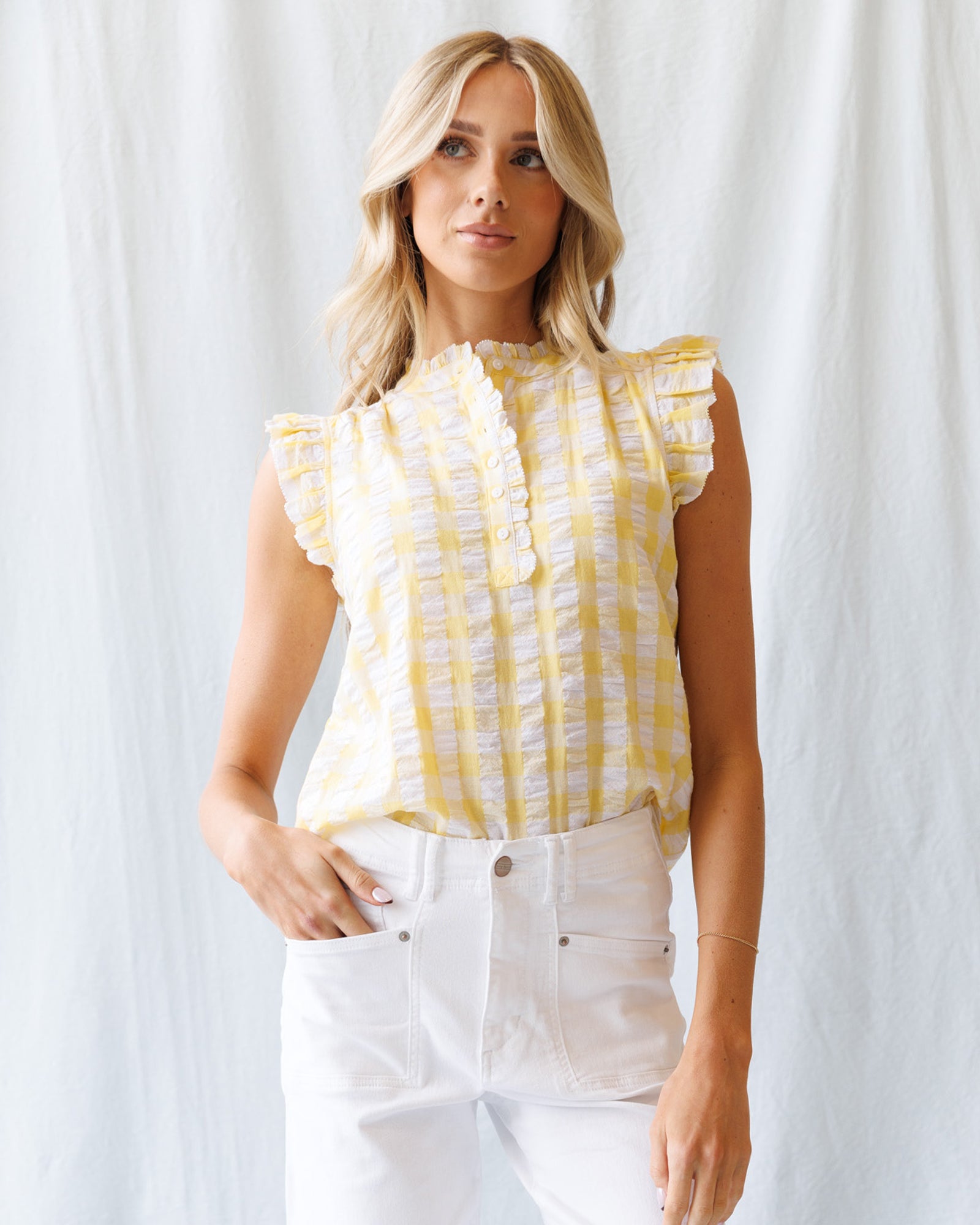 Woman wearing a yellow and white patterned top with white pants against a white background