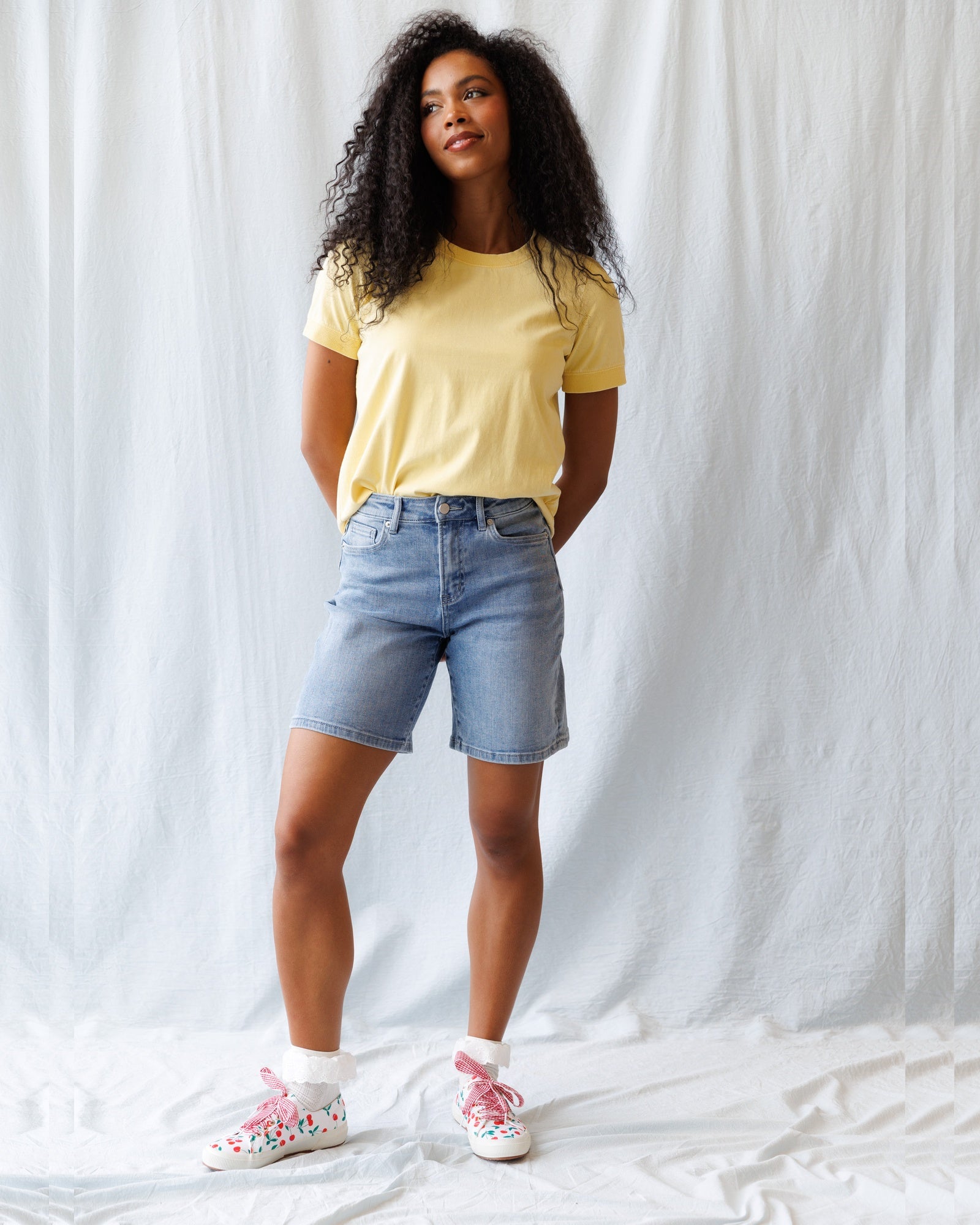 Woman wearing a yellow t-shirt and denim shorts against a white background