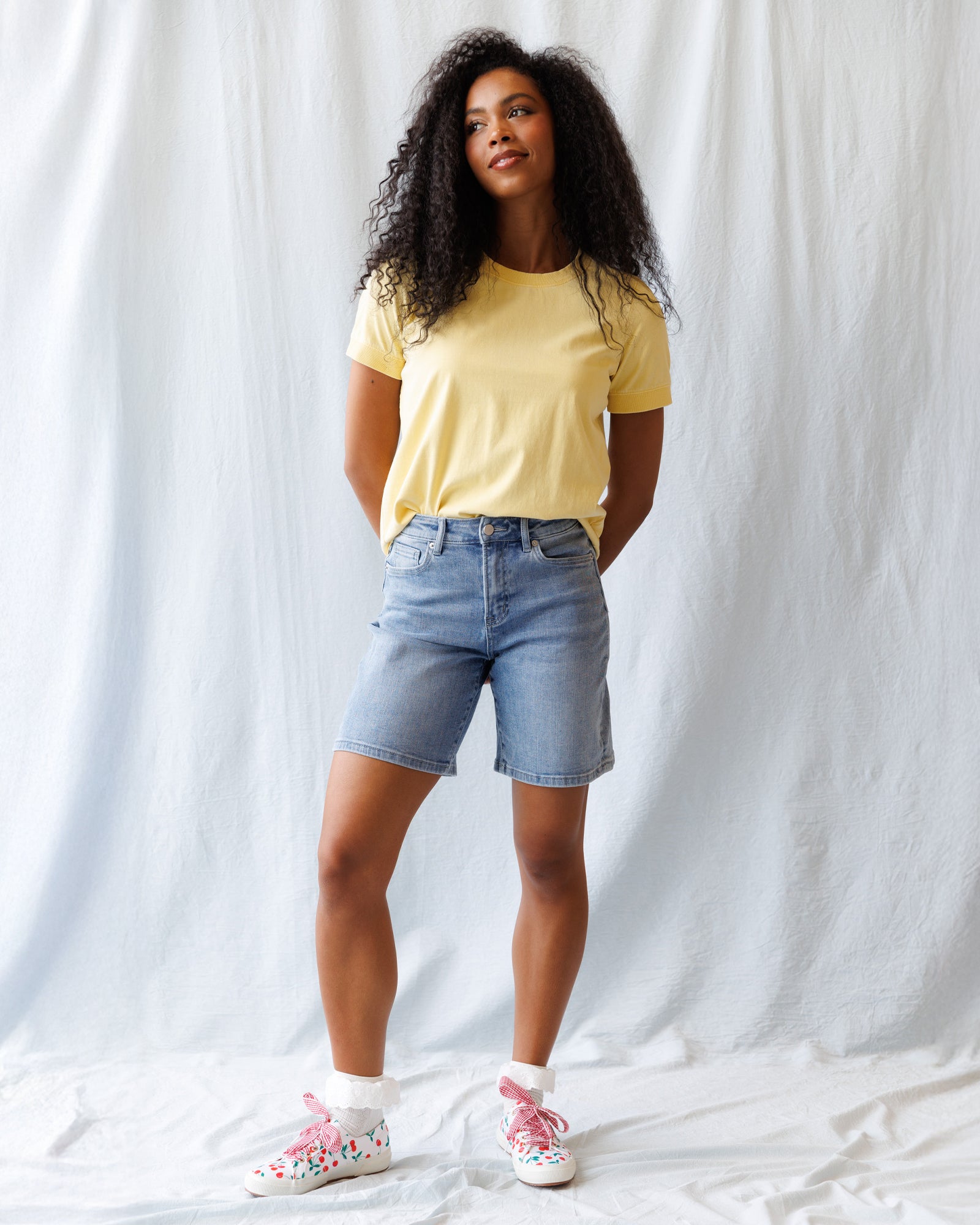 Woman wearing a yellow t-shirt and denim shorts against a white background