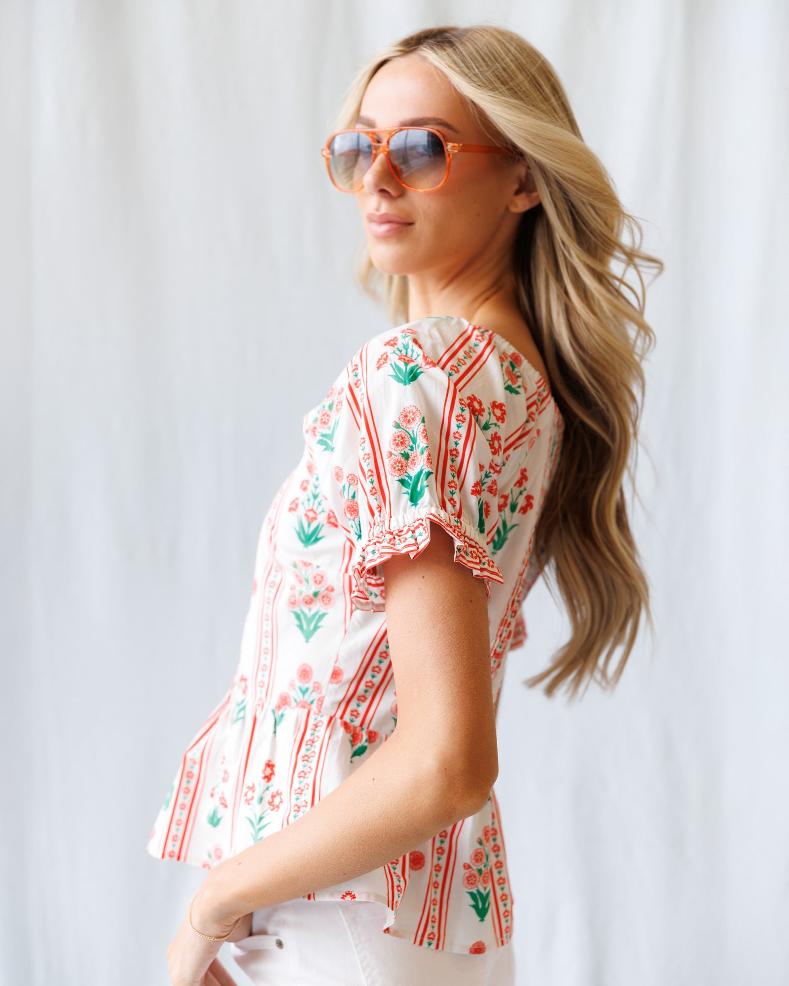 Woman wearing a floral blouse and sunglasses against a white background