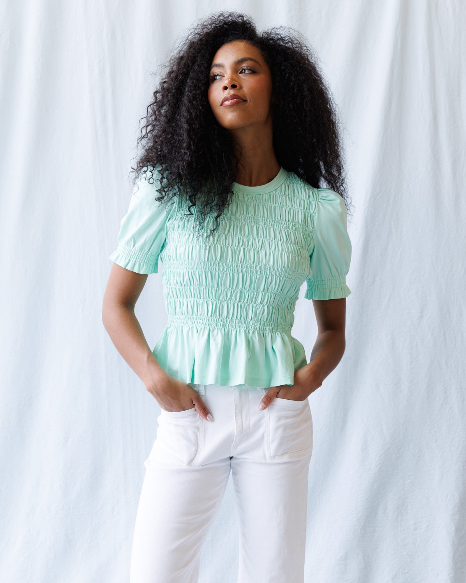 Woman wearing a light green top and white pants against a white background
