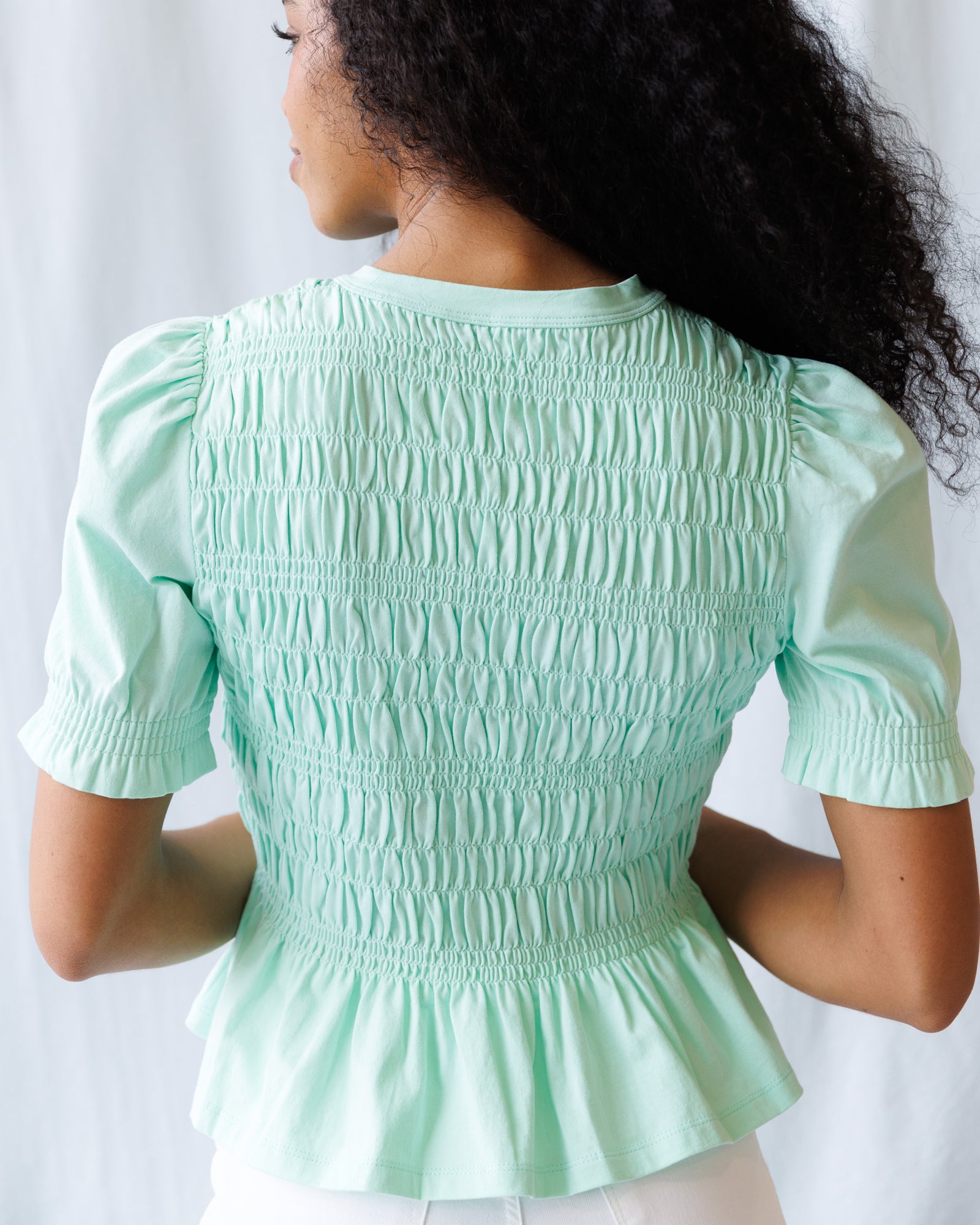 Person wearing a light green smocked blouse against a white background