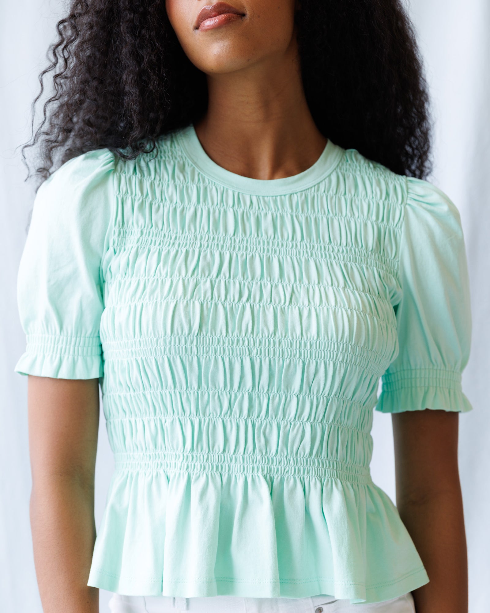 Woman wearing a light green smocked blouse against a white background