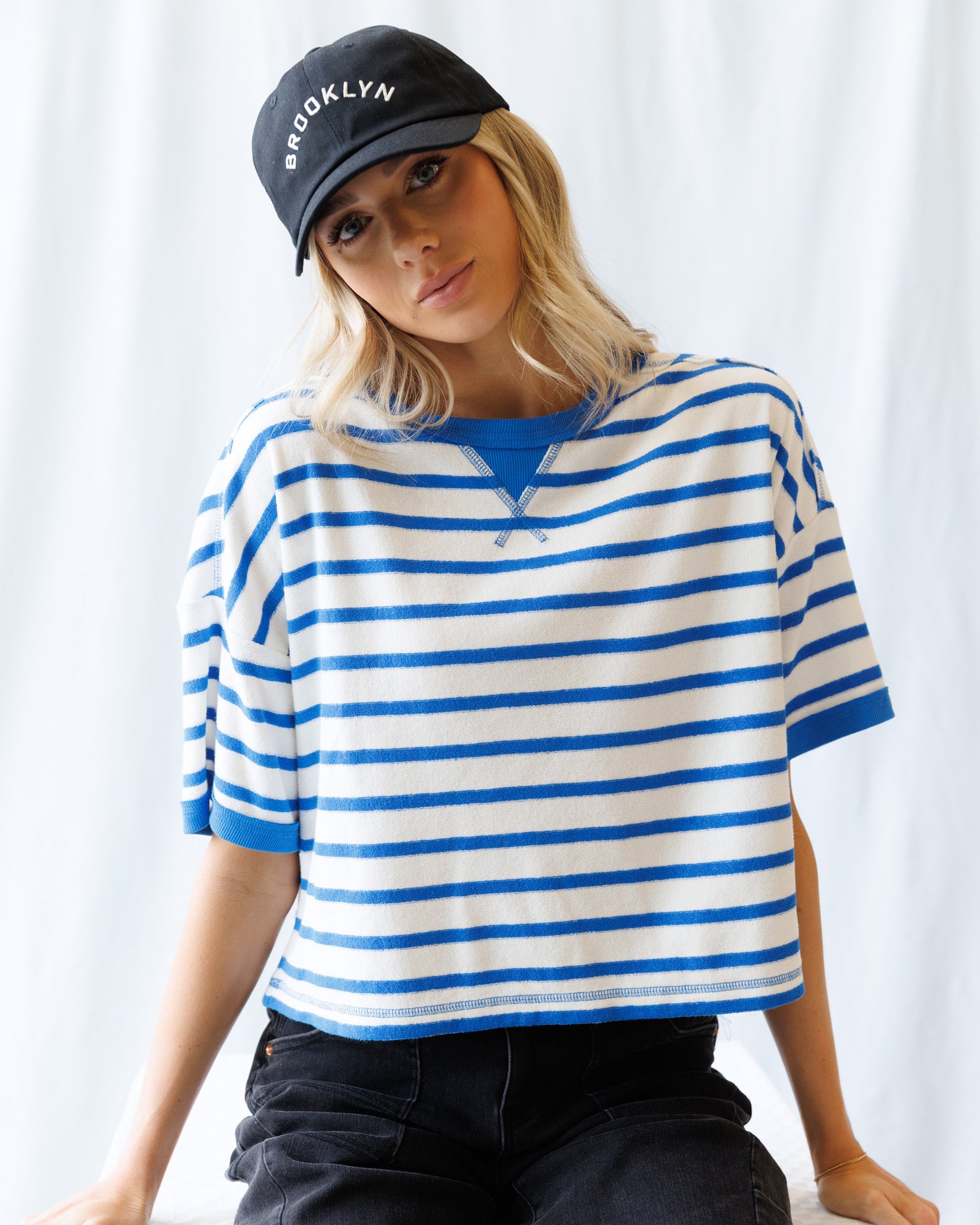 Woman wearing a blue and white striped shirt and a black cap with 'Brooklyn' text against a white background
