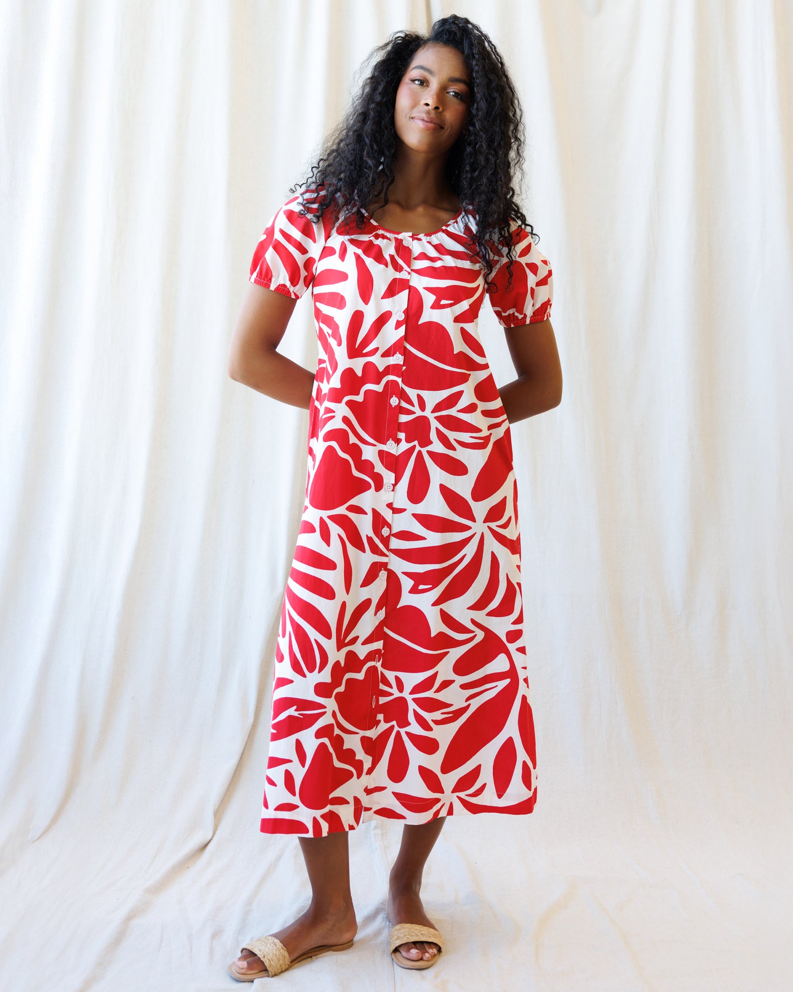 Woman wearing a red and white floral dress against a white curtain background