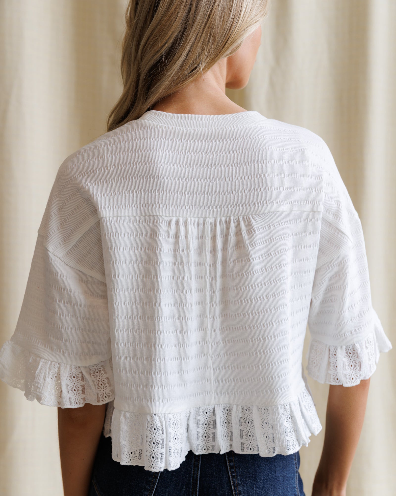 White blouse with lace details worn by a person against a neutral background