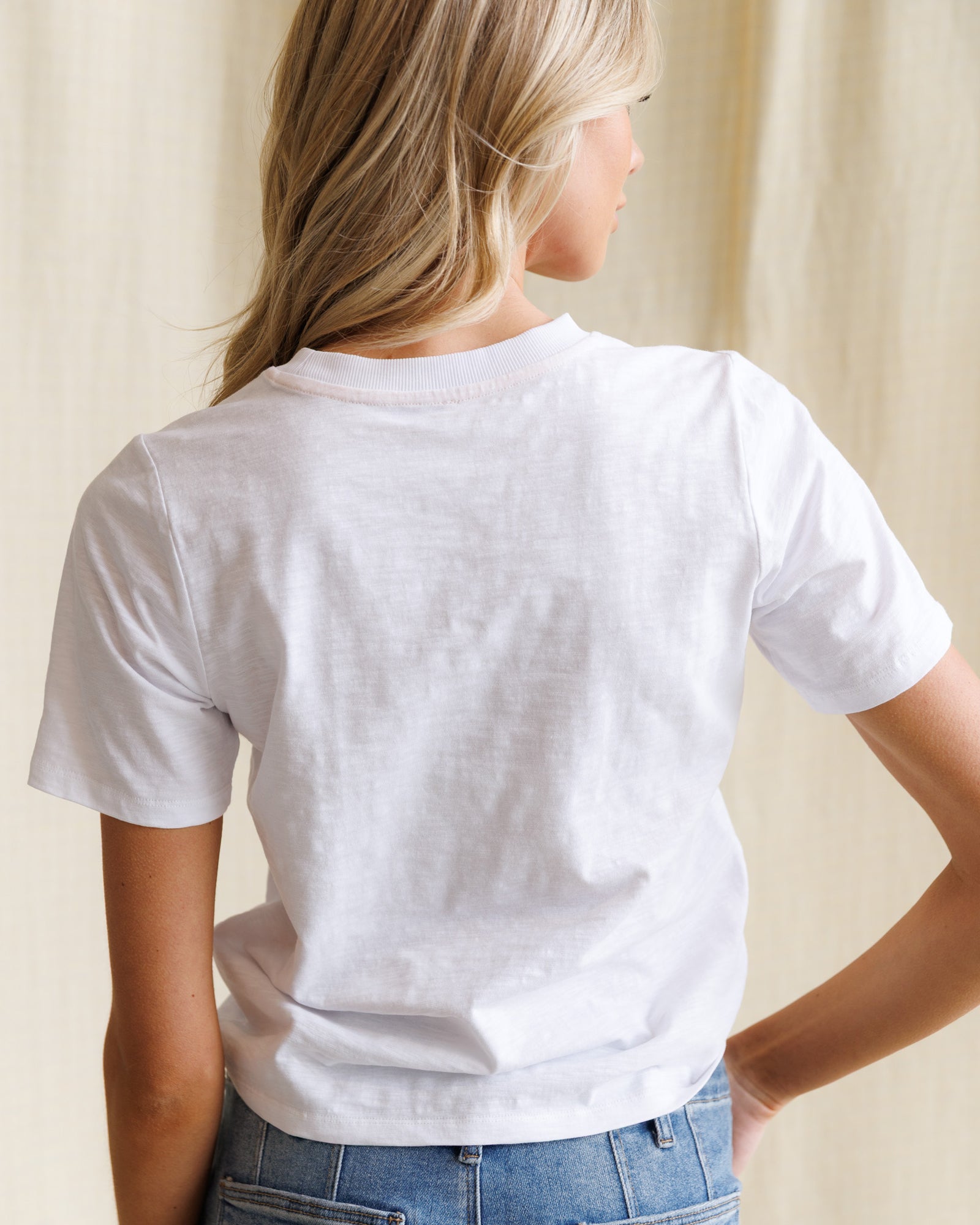 Person wearing a plain white t-shirt and blue jeans against a neutral background