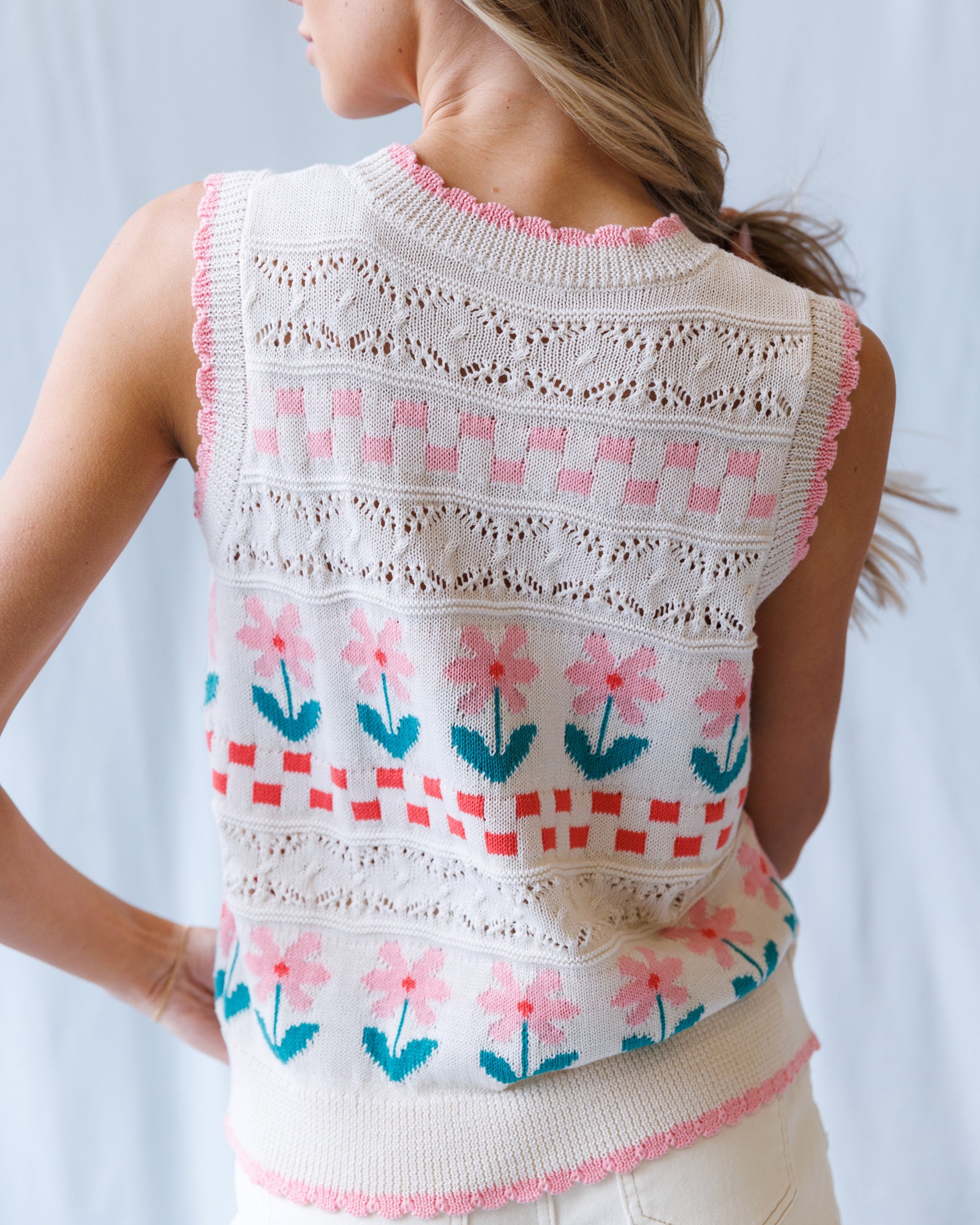 Woman wearing a sleeveless knitted top with floral patterns on a light background
