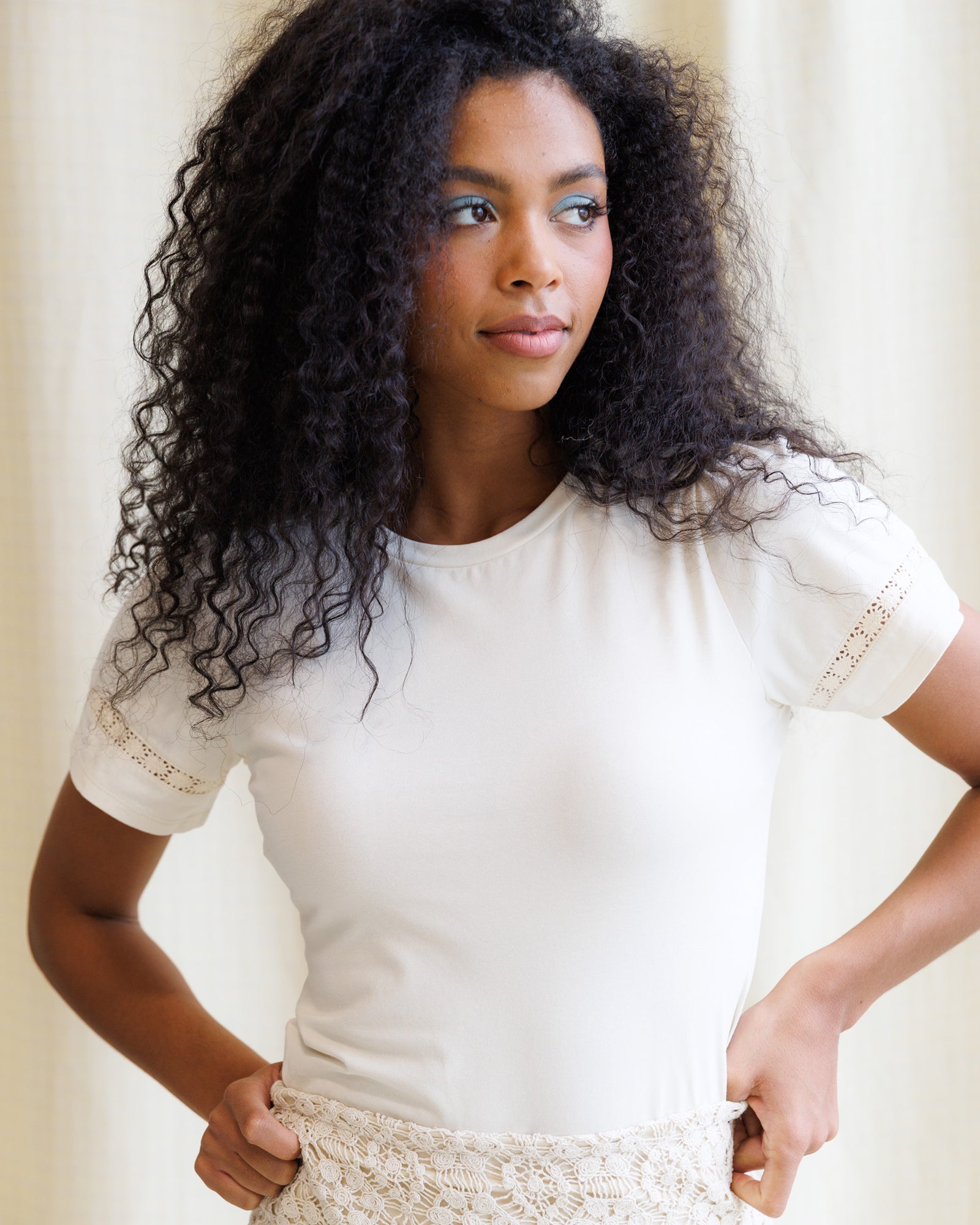 Woman wearing a white blouse with lace details against a neutral background