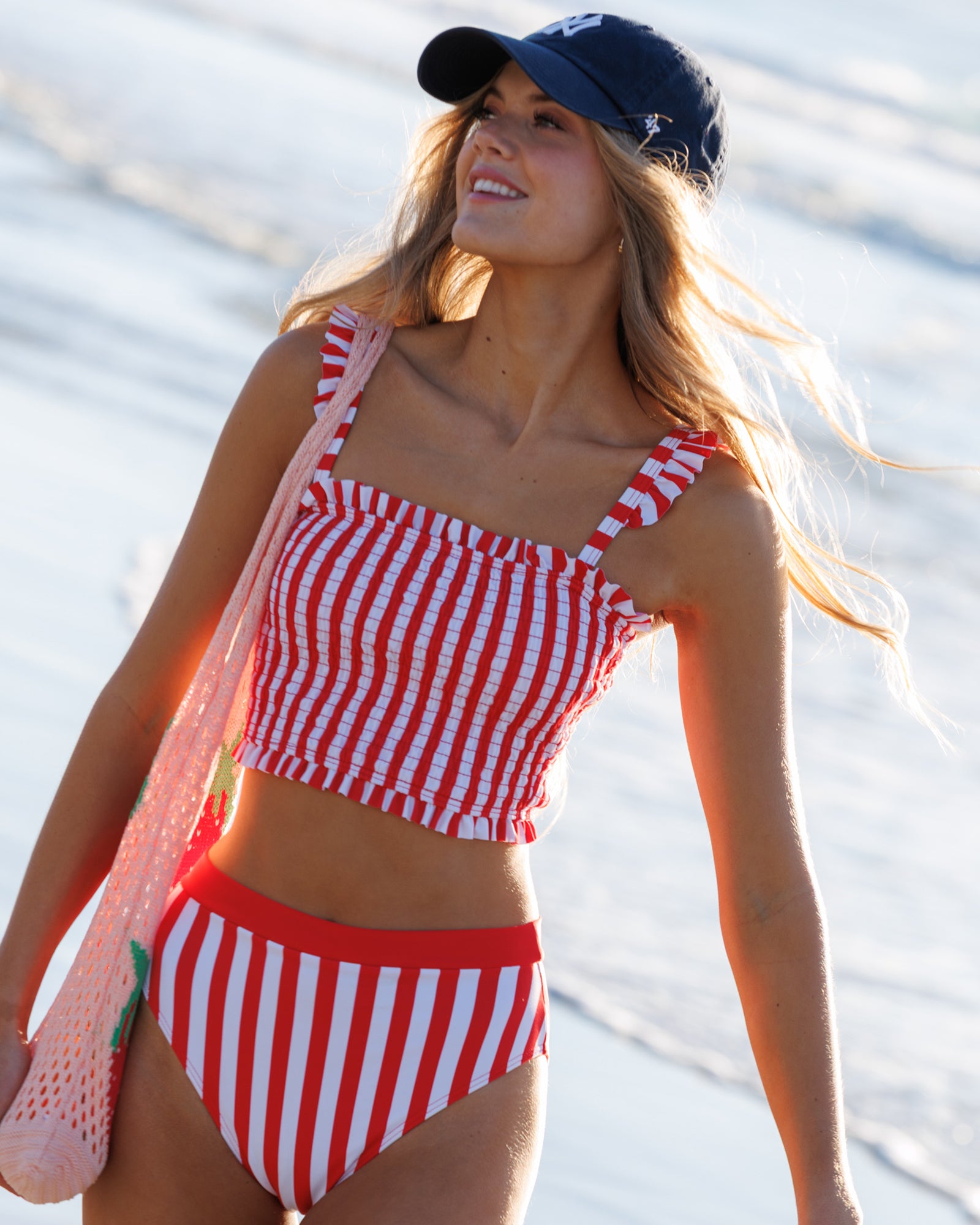 Woman wearing a red and white striped bikini with a matching cap, standing by water.