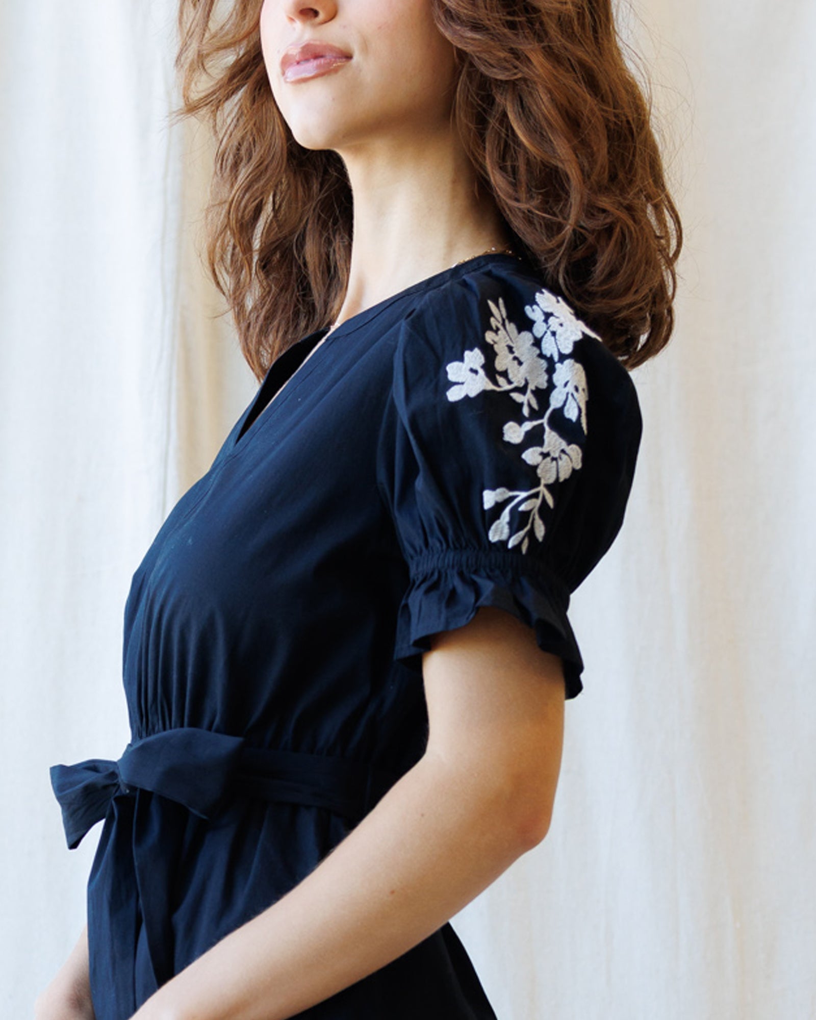 Woman wearing a navy blue dress with white floral embroidery on a white background