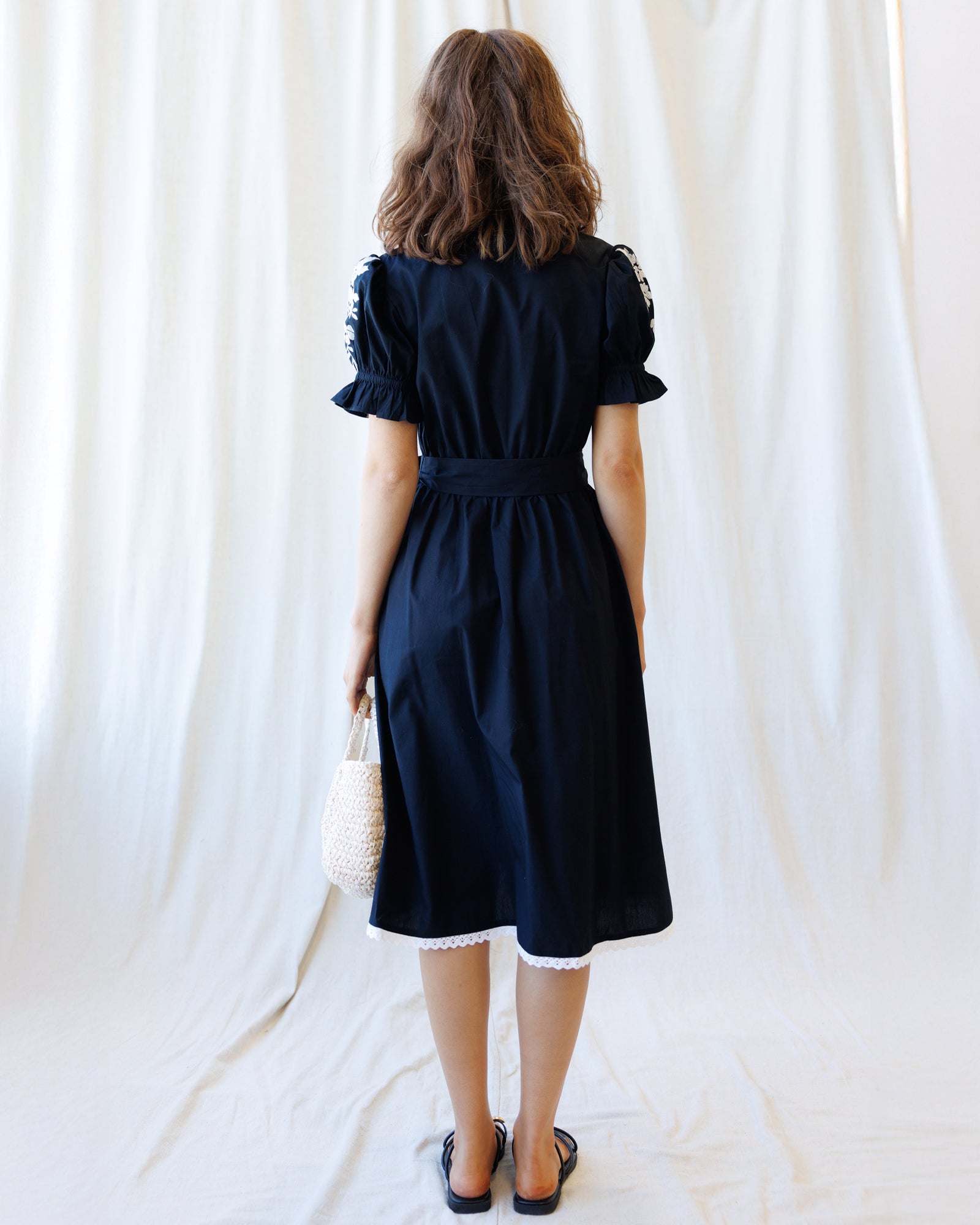 Woman wearing a black dress against a white curtain backdrop