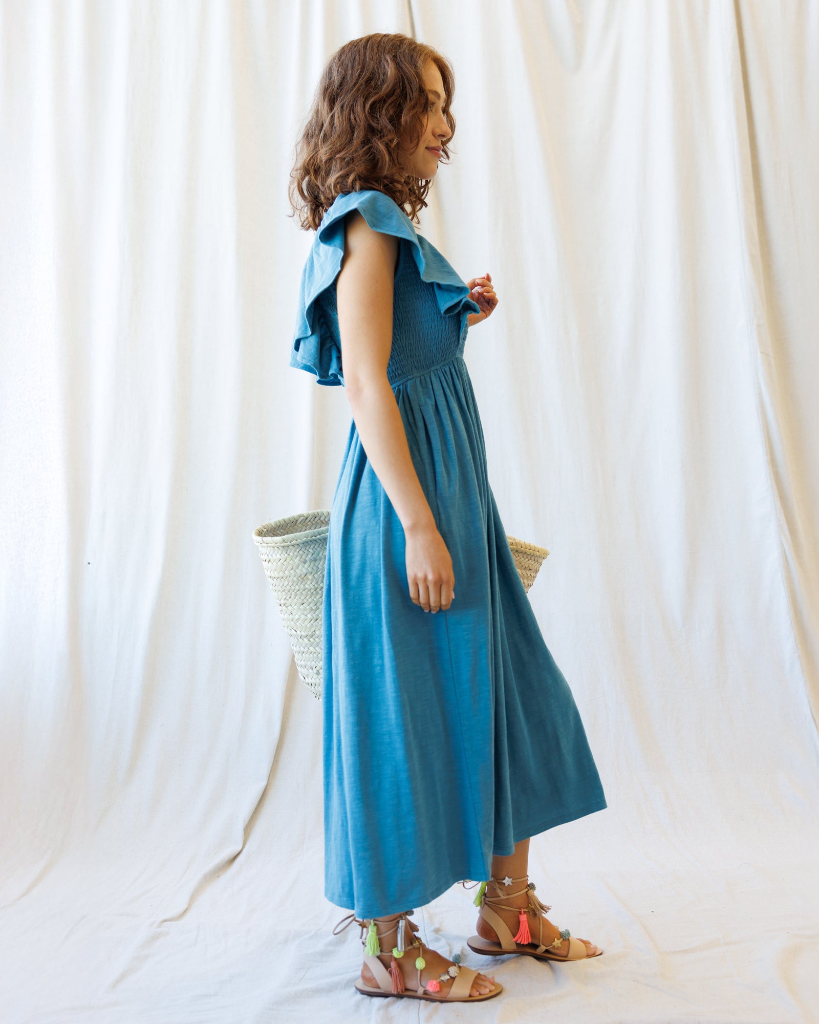 Woman wearing a blue dress standing against a white curtain