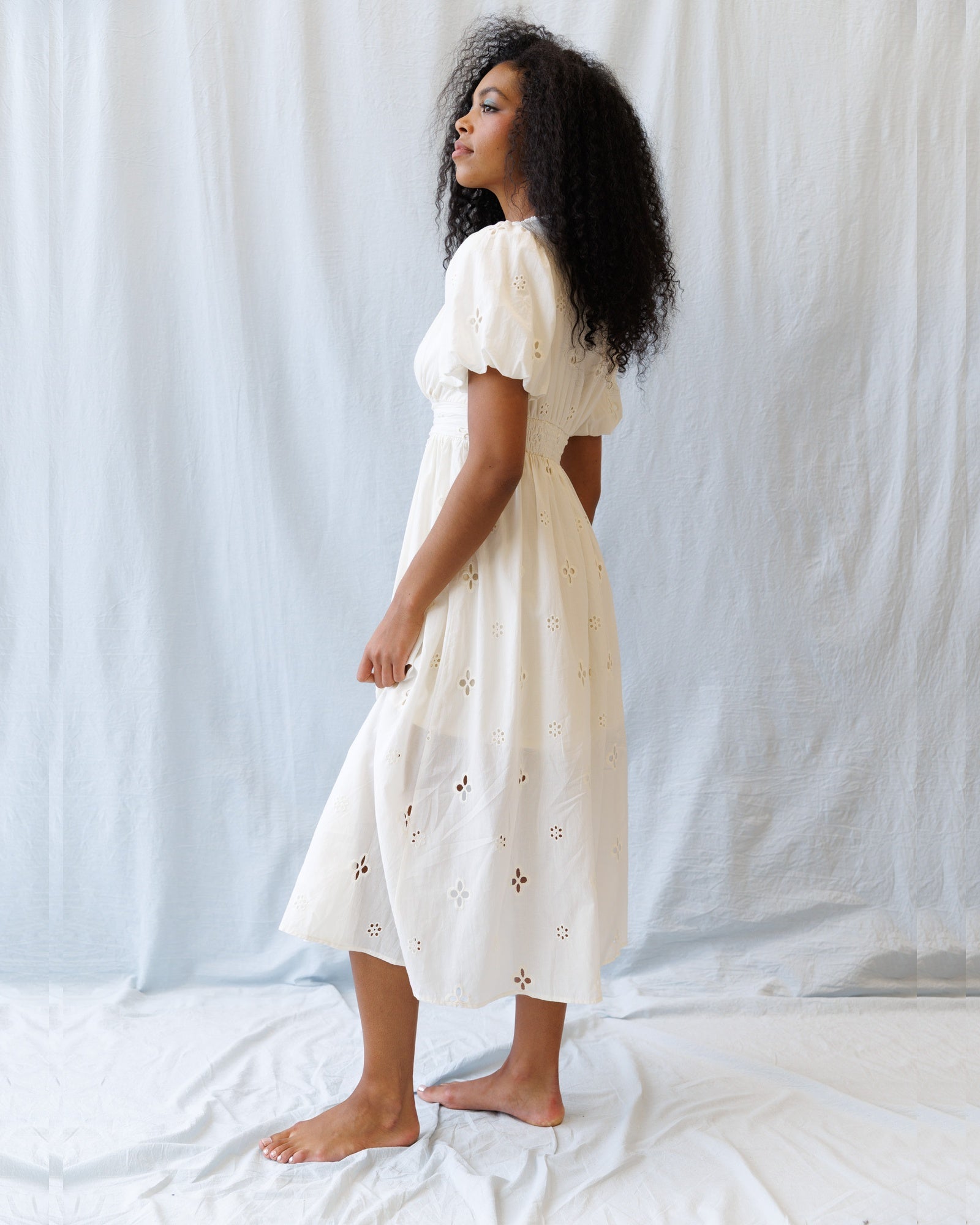 Woman wearing a white dress with floral patterns against a plain background