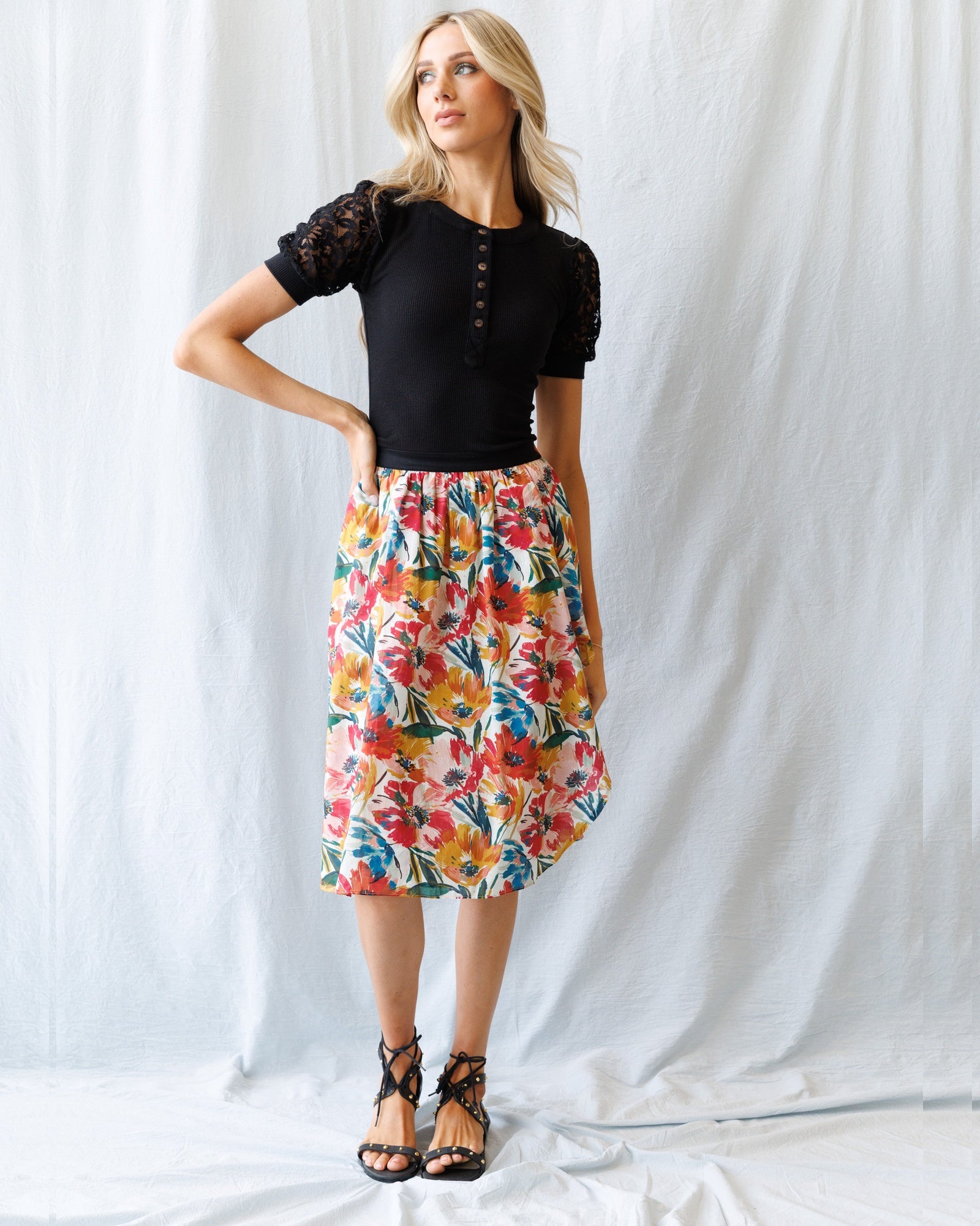 Woman wearing a black top and colorful floral skirt against a white background