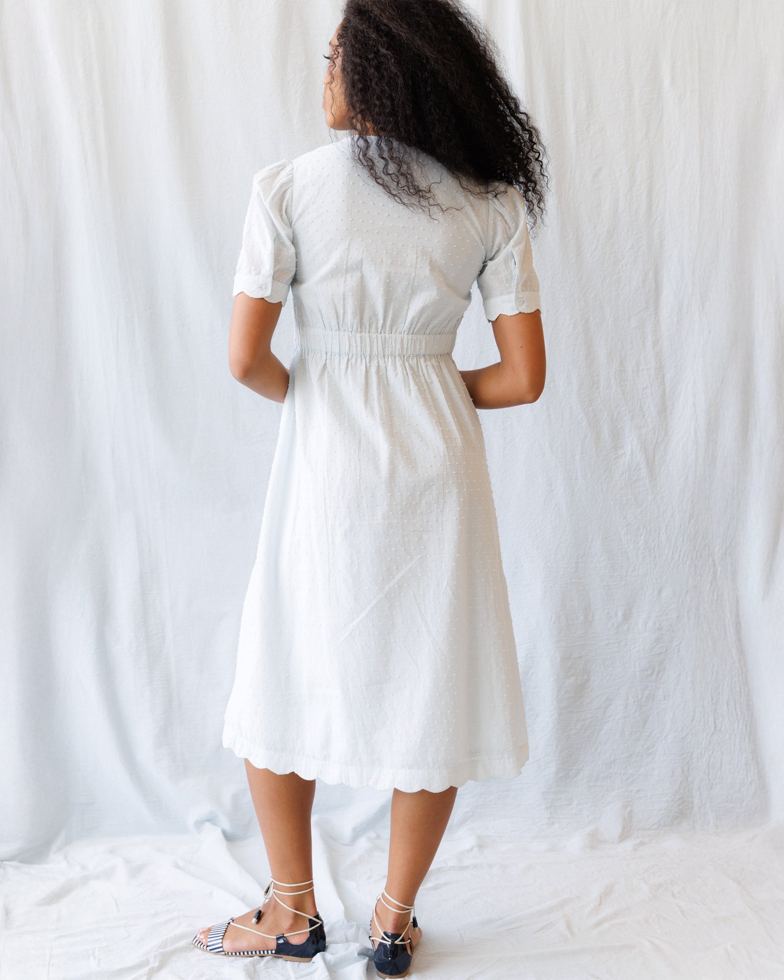 Woman wearing a light blue dress standing against a plain white background