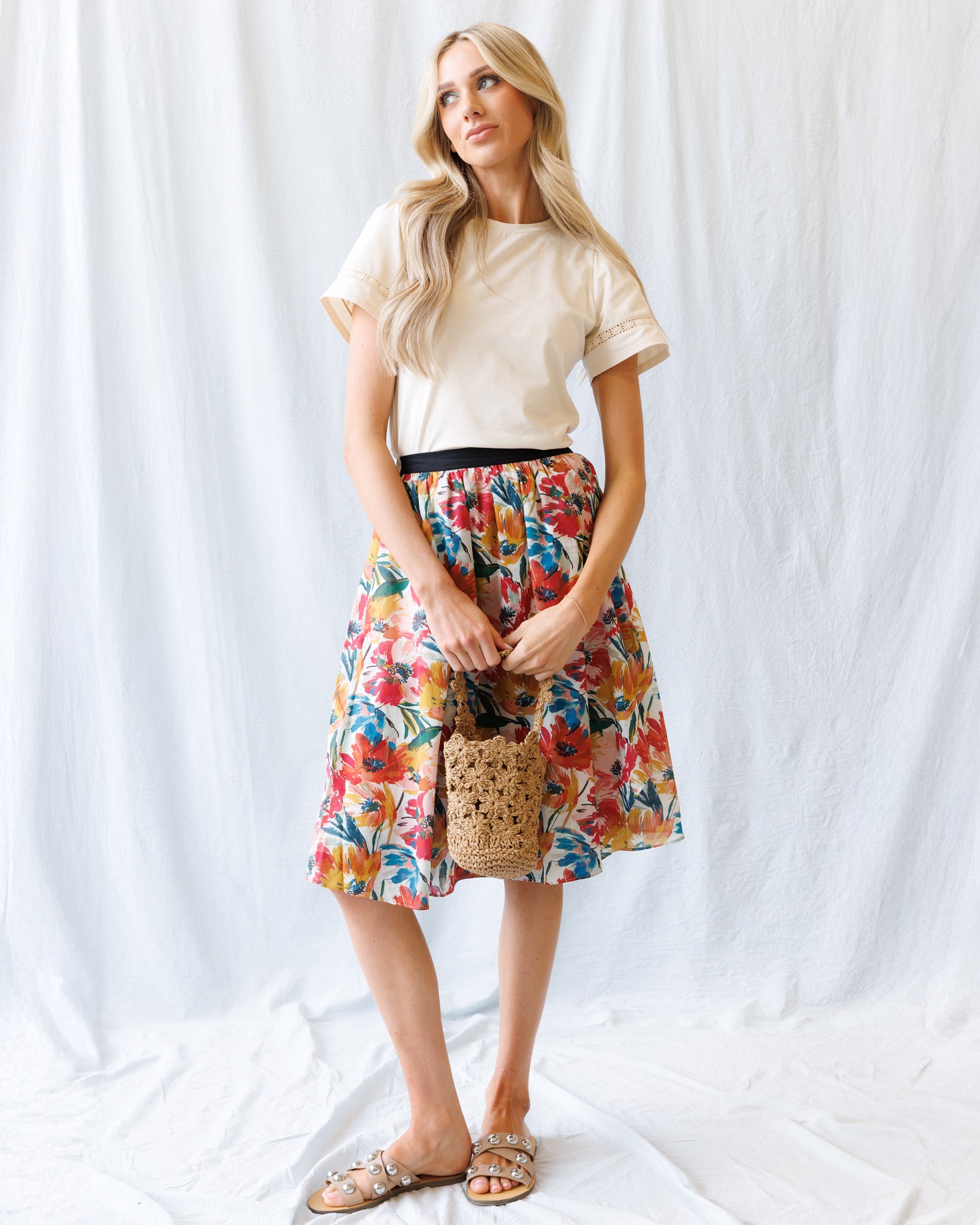 Woman wearing a colorful floral skirt and beige top against a white background