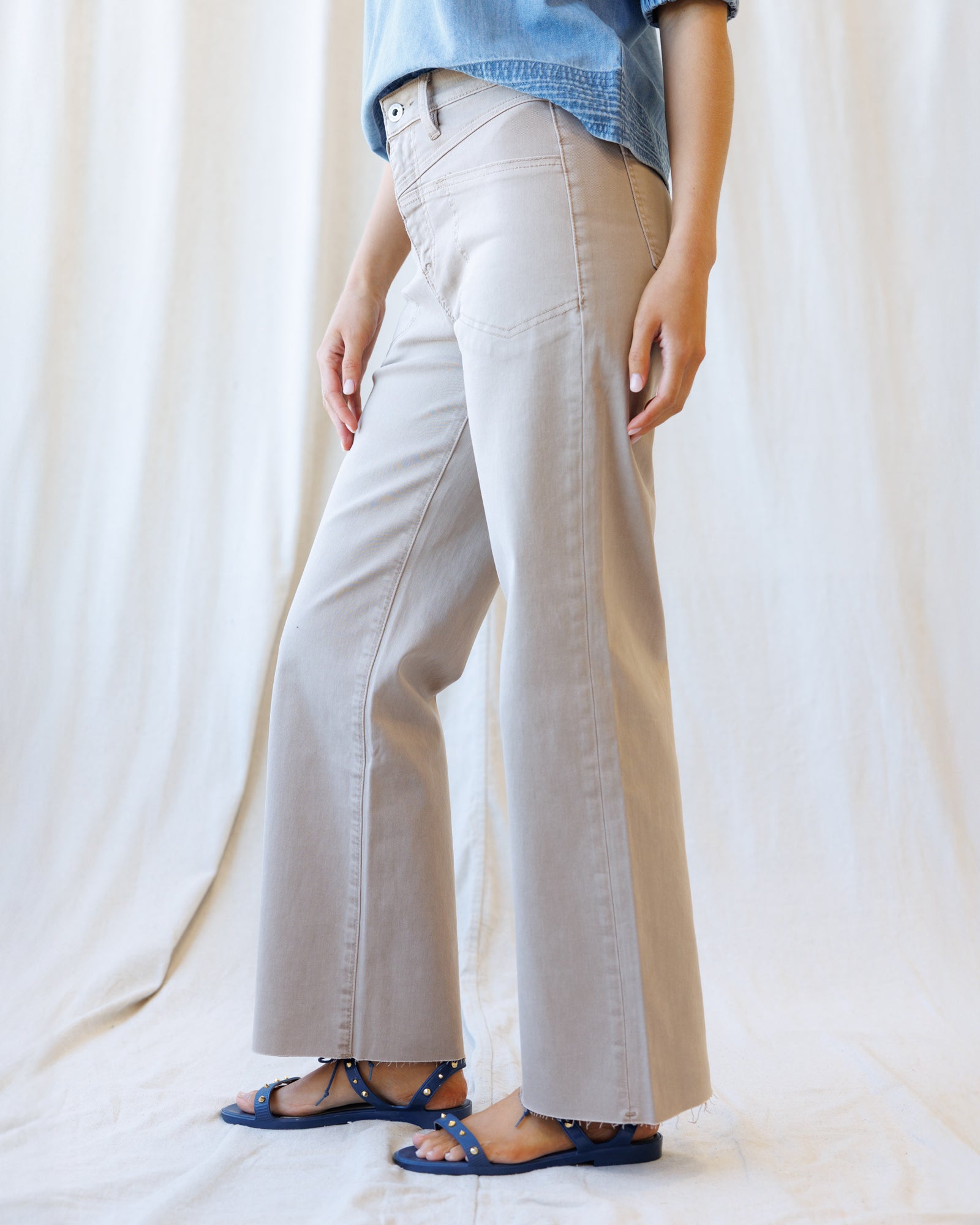 Person wearing beige wide-leg pants and a blue denim shirt on a white background