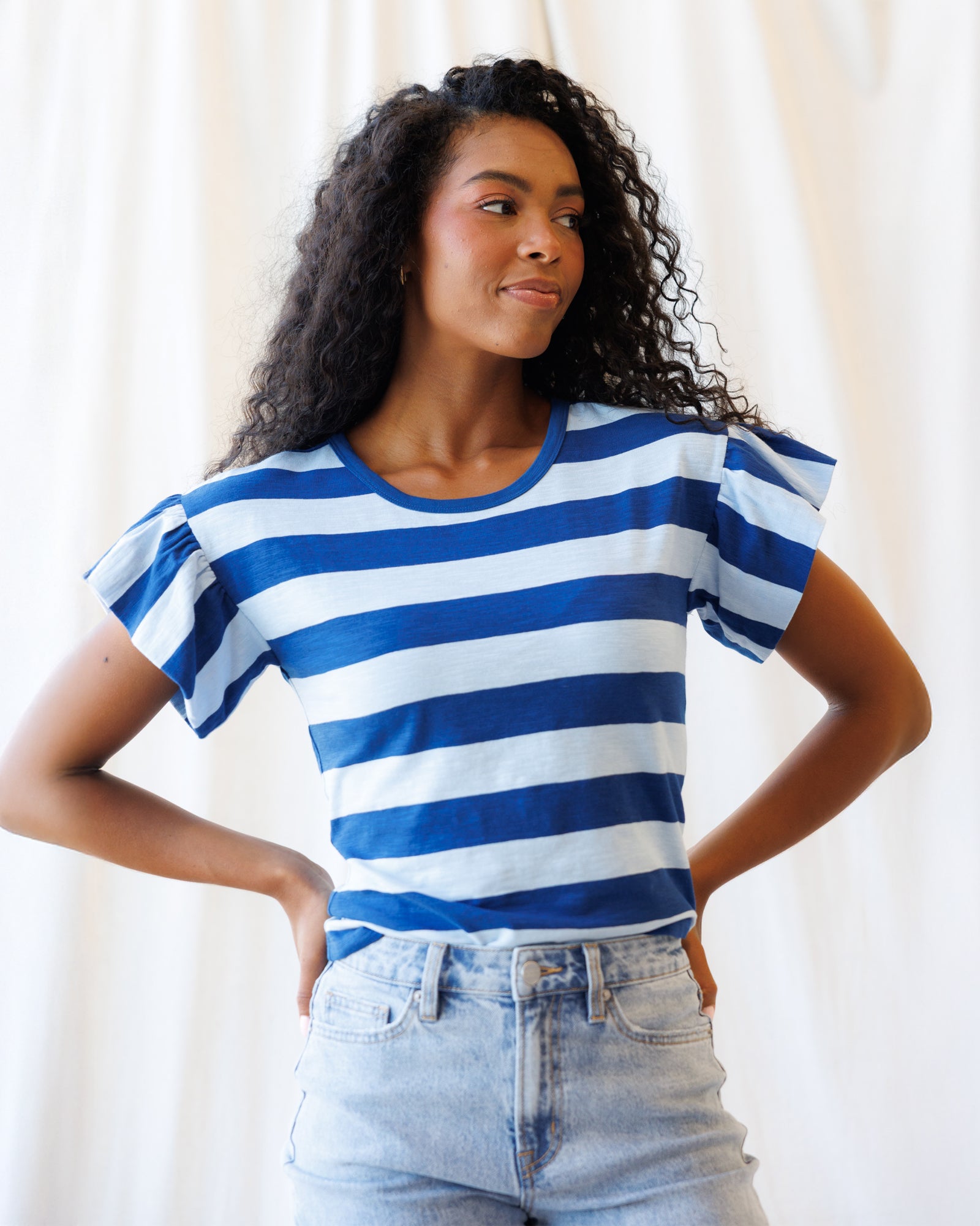Woman wearing a blue and white striped shirt with ruffled sleeves against a plain background