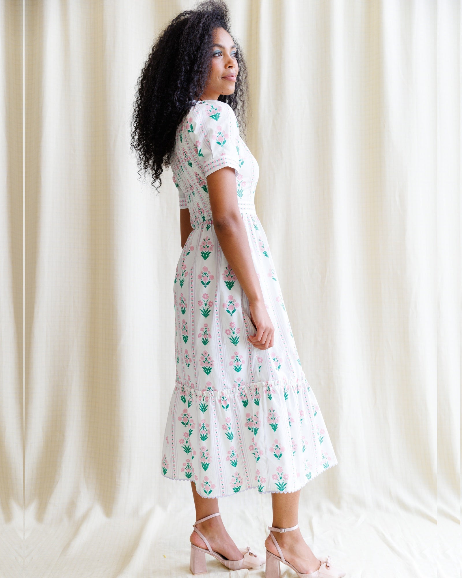 Woman wearing a white dress with floral pattern against a plain background