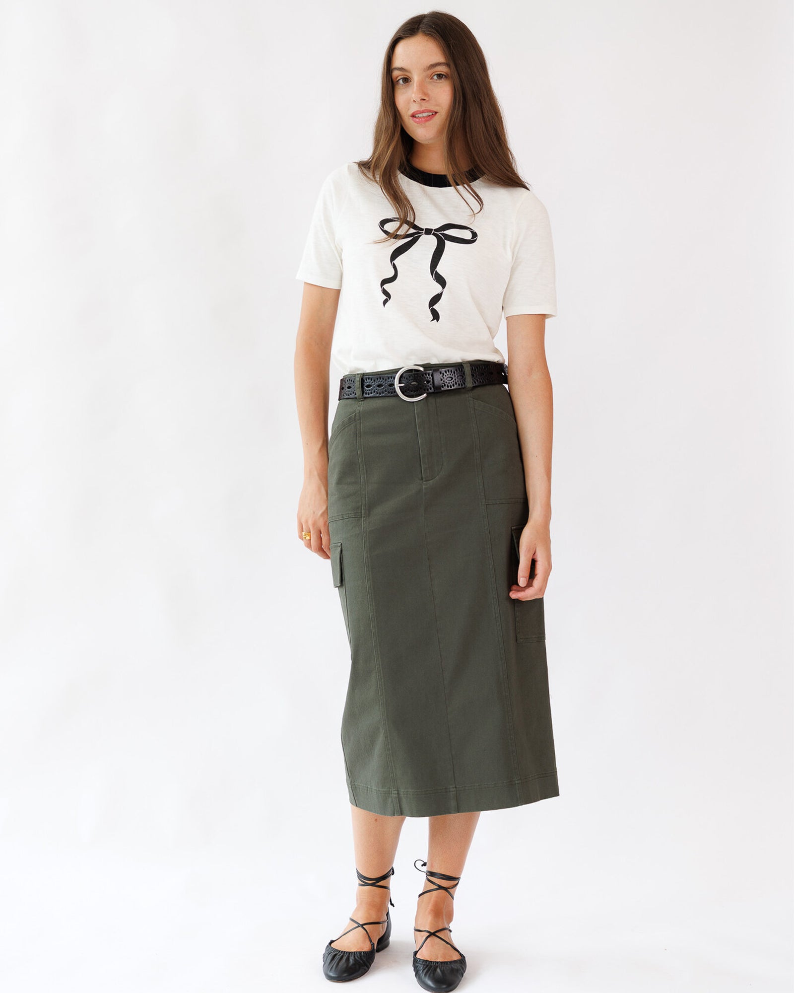 Woman wearing a white top with black bow and green skirt on a white background