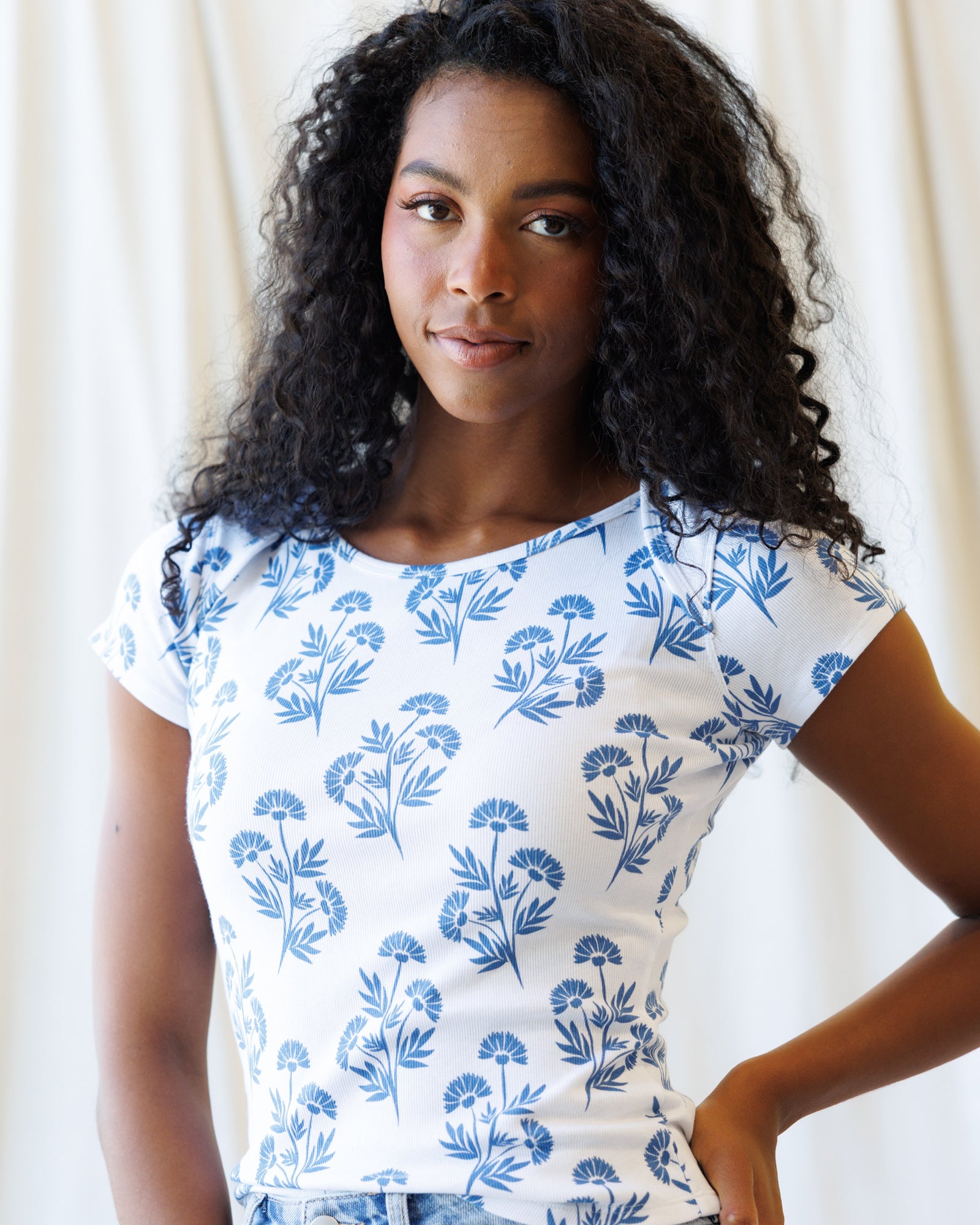 Woman wearing a white t-shirt with blue floral pattern against a plain background