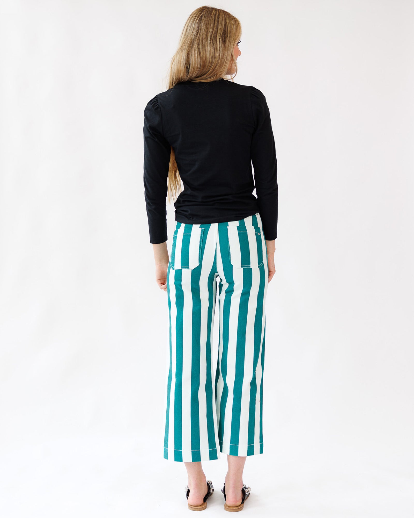 Woman wearing black long-sleeve top and green and white striped pants on a white background