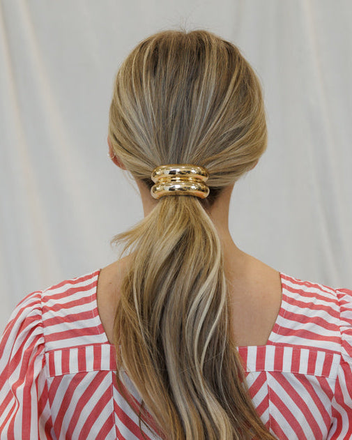 Person wearing a red and white striped dress with a gold hair accessory, standing against a plain background.