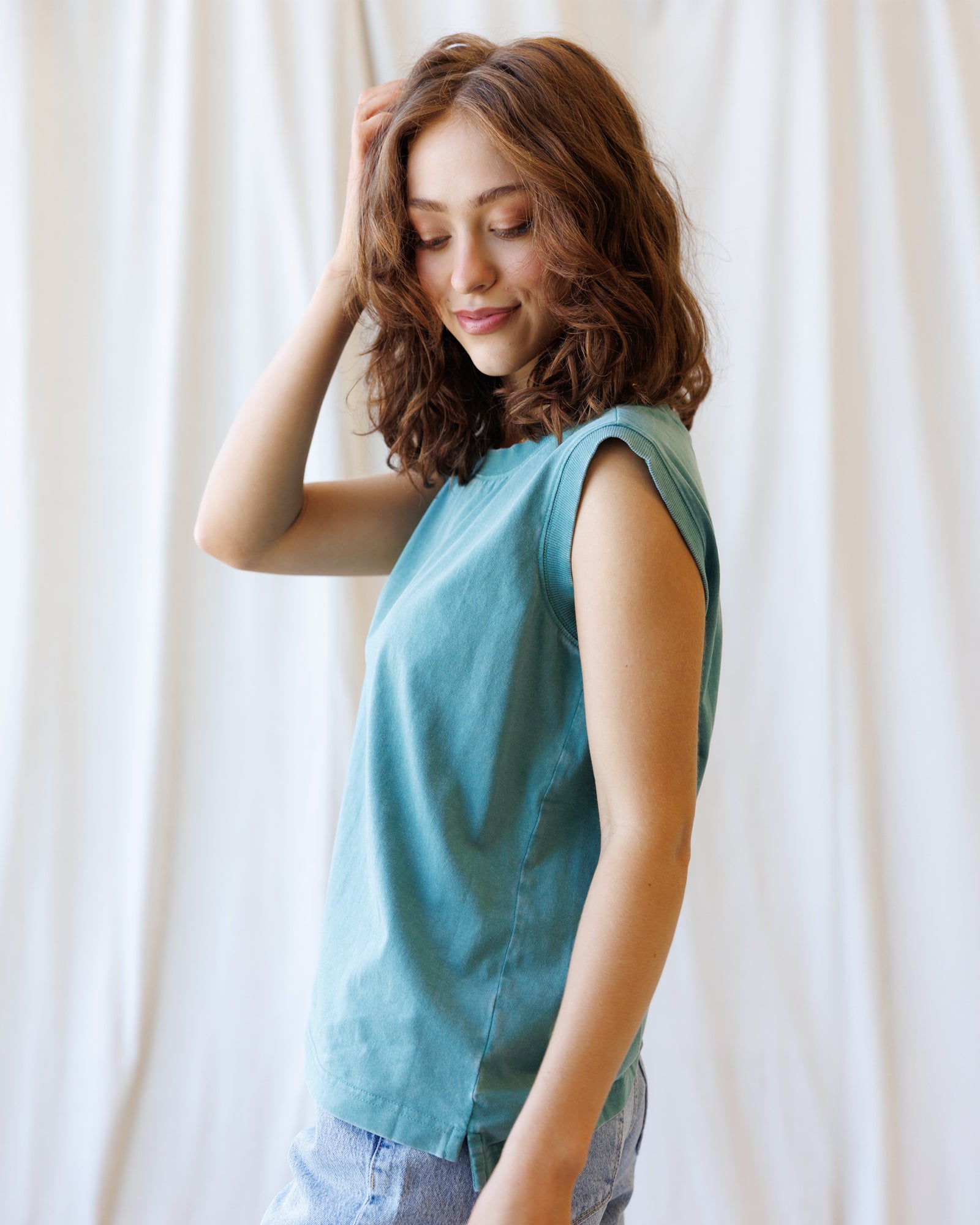 Woman wearing a teal sleeveless top against a white curtain background