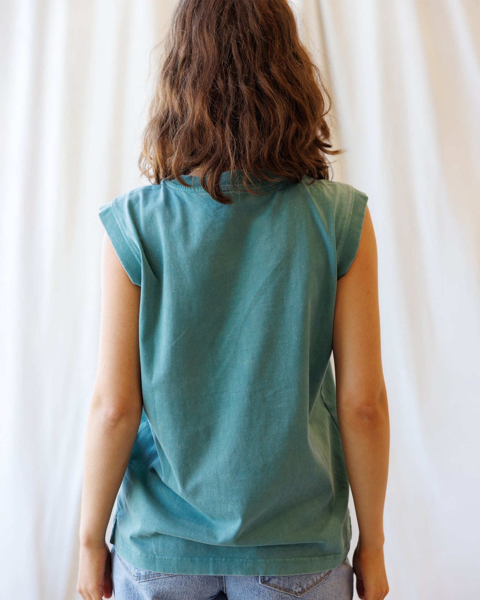 Person wearing a teal sleeveless top against a white curtain background