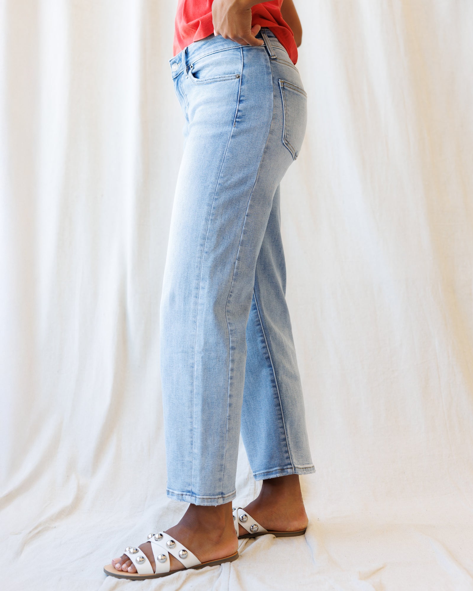 Person wearing light blue jeans and white sandals on a plain background