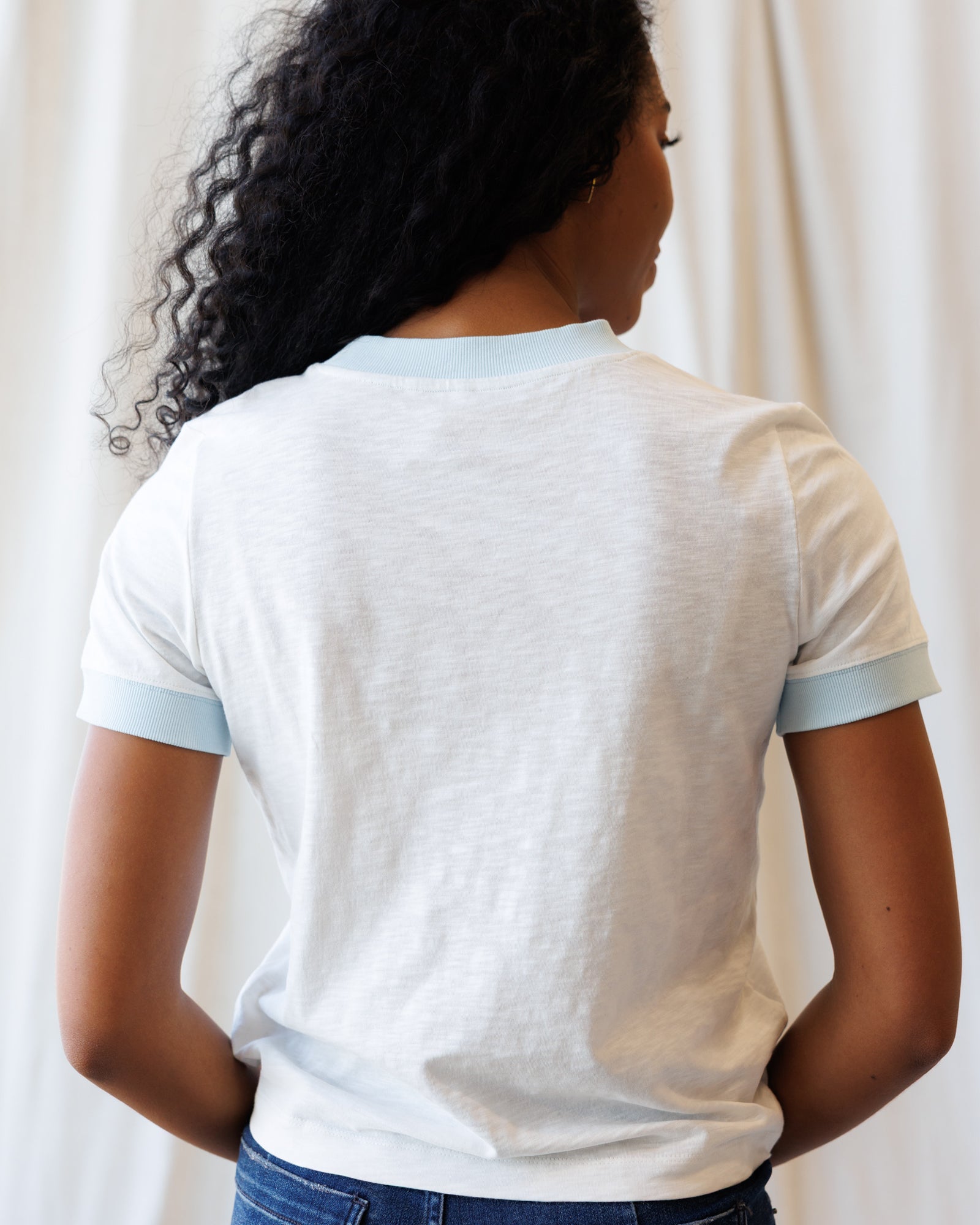 Person wearing a white t-shirt with blue trim against a plain background
